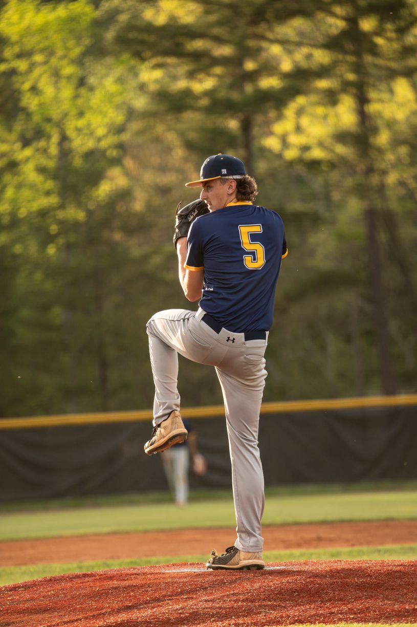 Baseball pitcher in navy uniform winds up for a pitch on a sunlit baseball field.