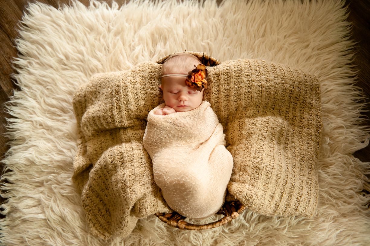 Newborn baby wrapped in soft beige blankets on furry white backdrop.