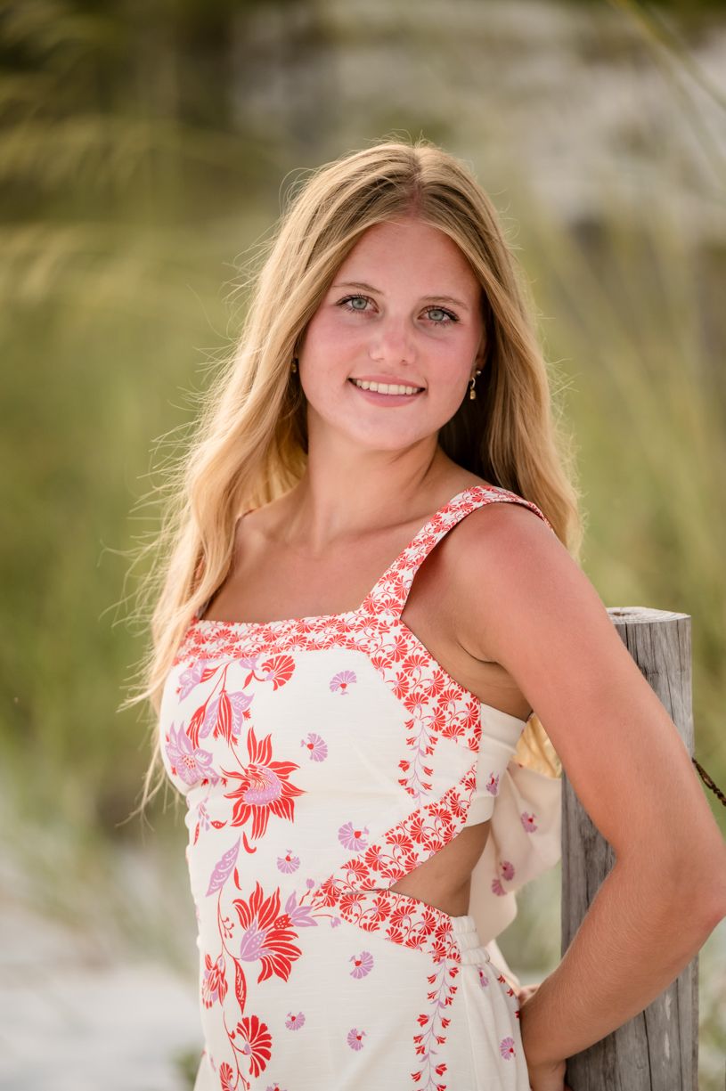 A senior girl standing against a natural background wearing a floral print top.