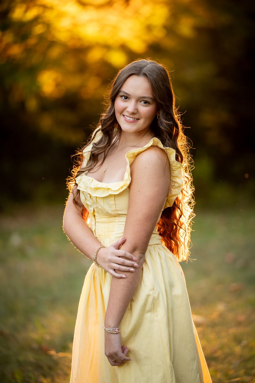 A senior girl wearing a yellow sundress portrait session with golden backlight in nature.