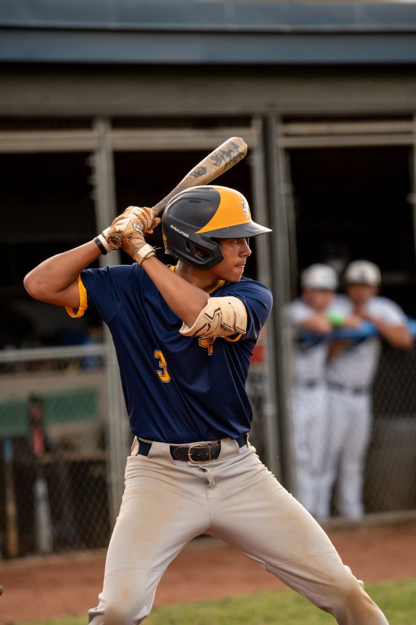 Baseball players in navy uniforms demonstrate batting stances during a game.