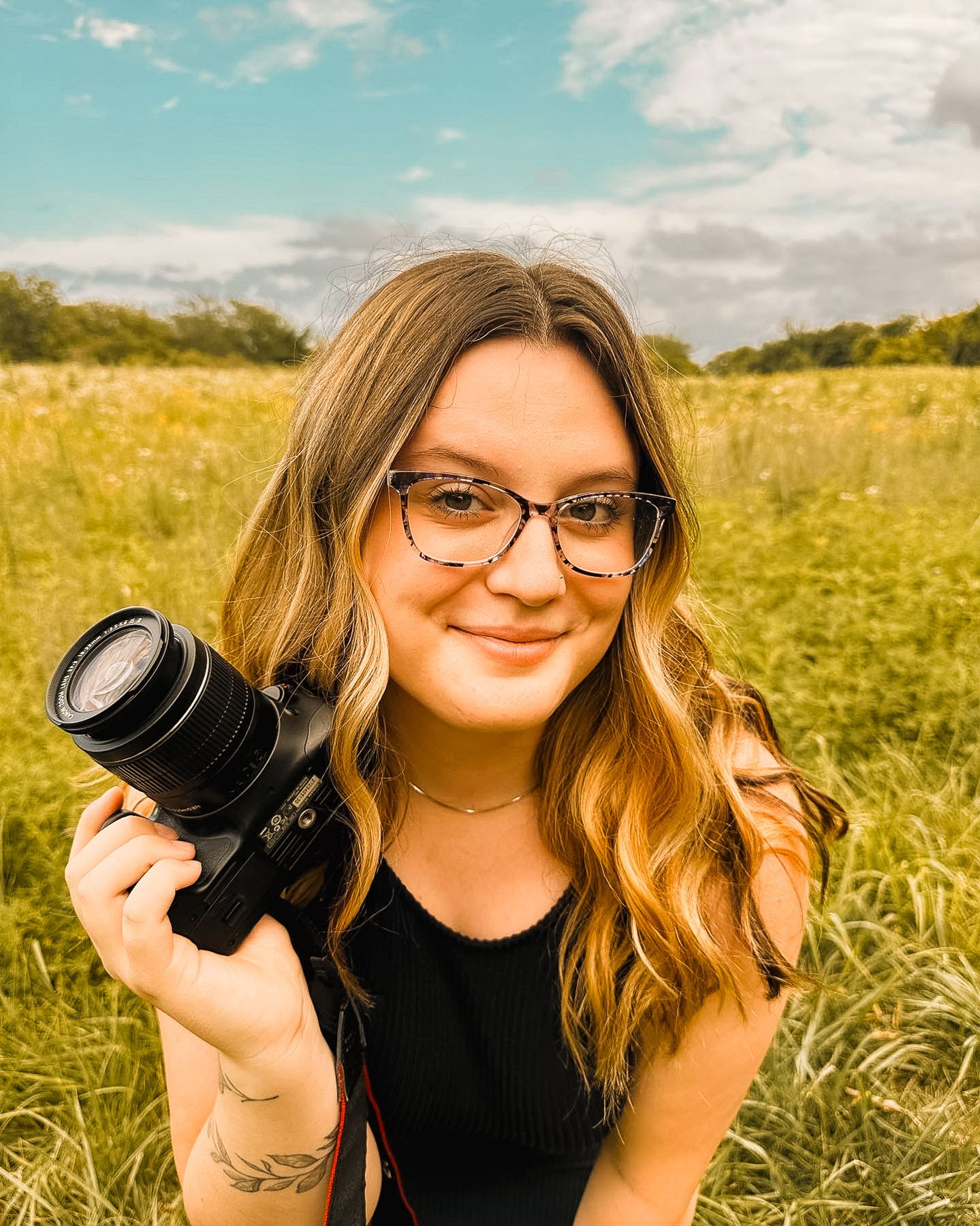 Portrait of photographer holding DSLR camera in golden wildflower field.