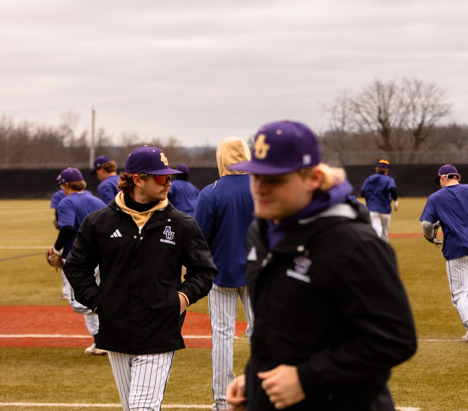 Baseball team members in black jackets and pinstripes gather on field during practice.