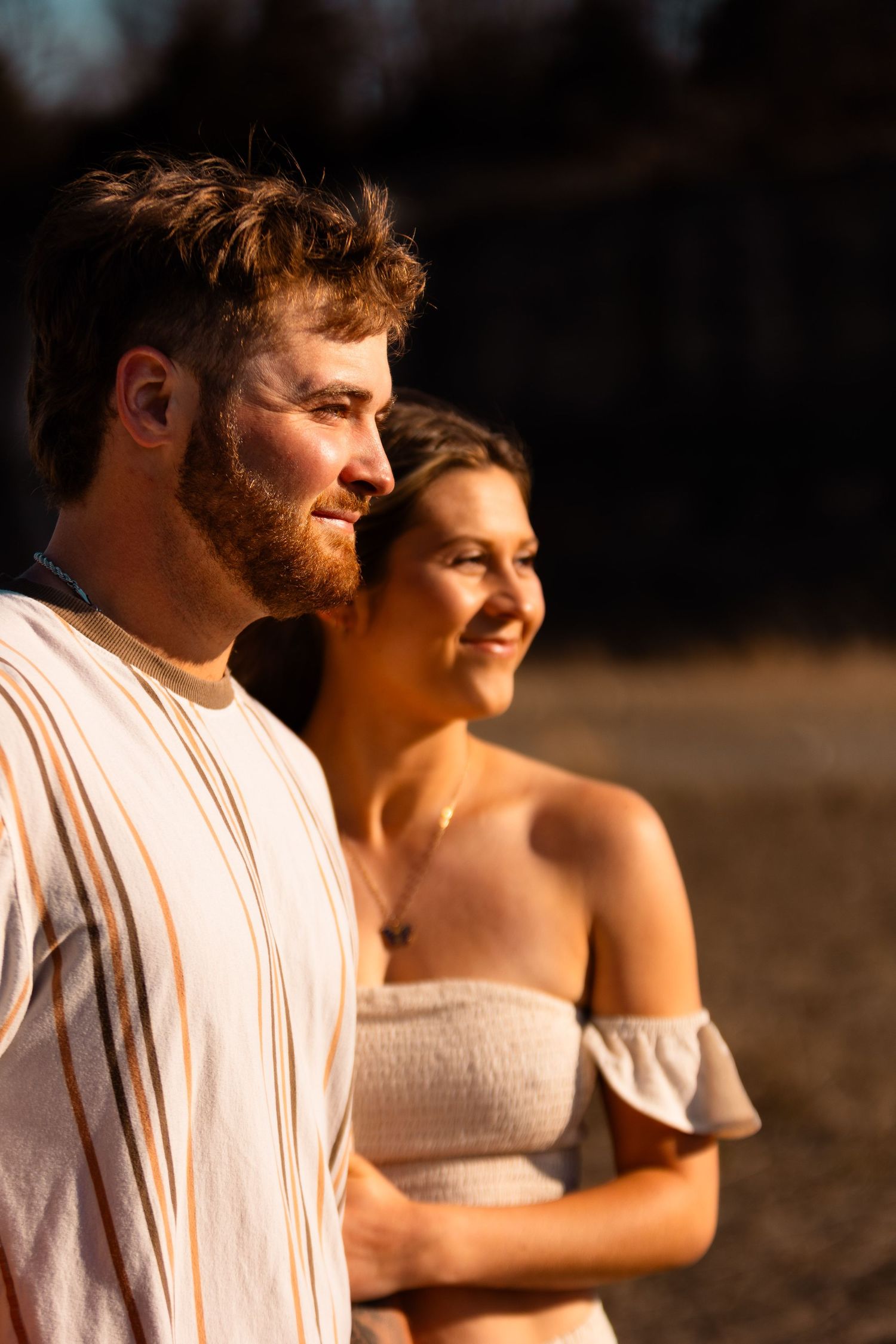 Couple in white clothing smiling while standing in warm sunset light.