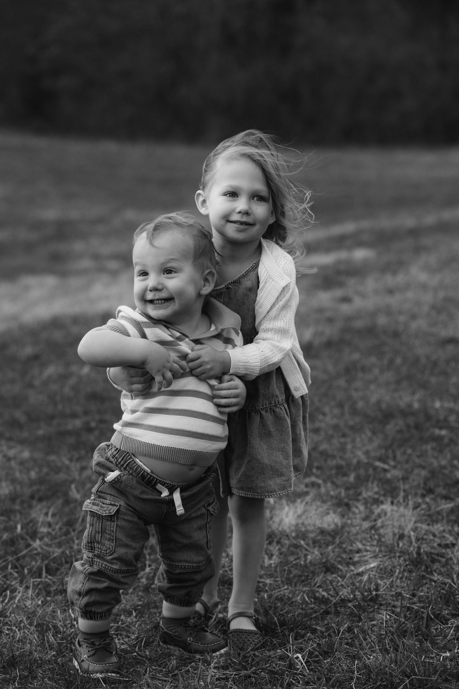 Two children play together on grassy field in black and white.