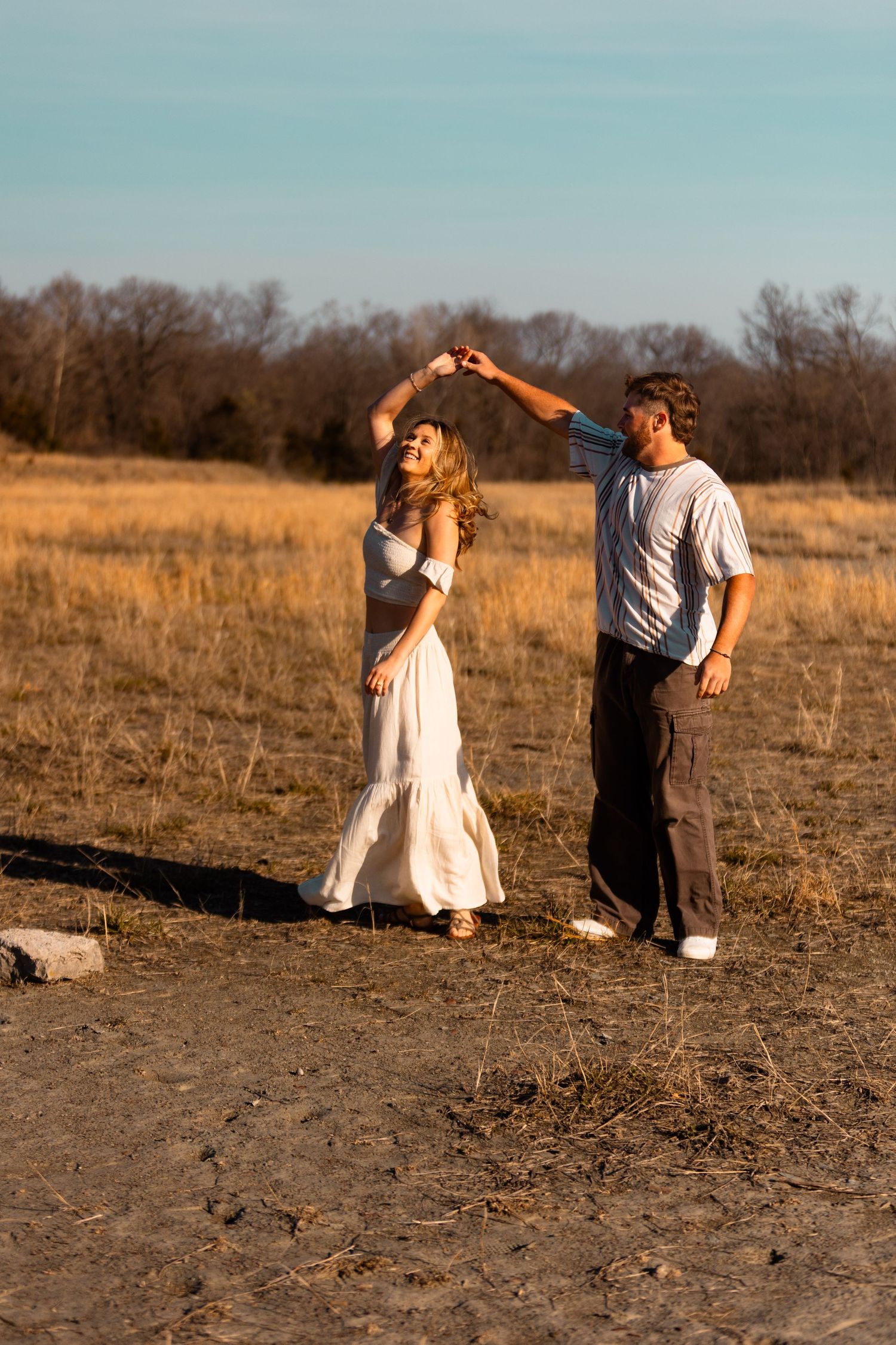 Couple dancing together in a field during golden hour with cliffs in background.