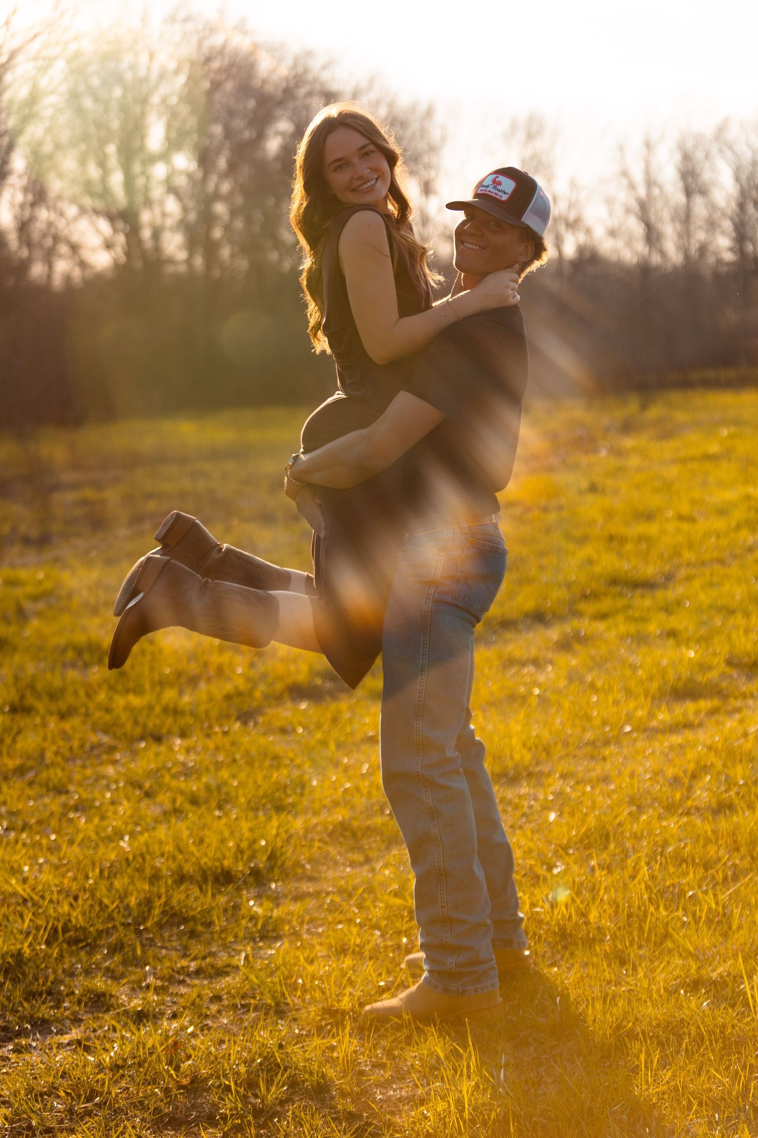 Couple dances and embraces in sunlit field during sunset.