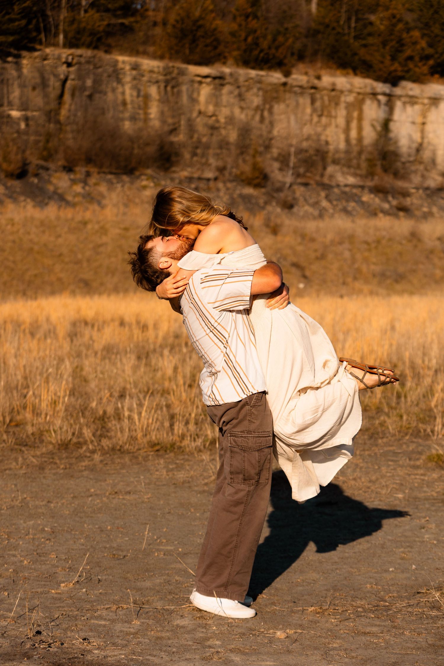 A person in a light colored shirt performs a dynamic dance move against a rustic stone wall and grassy field background.