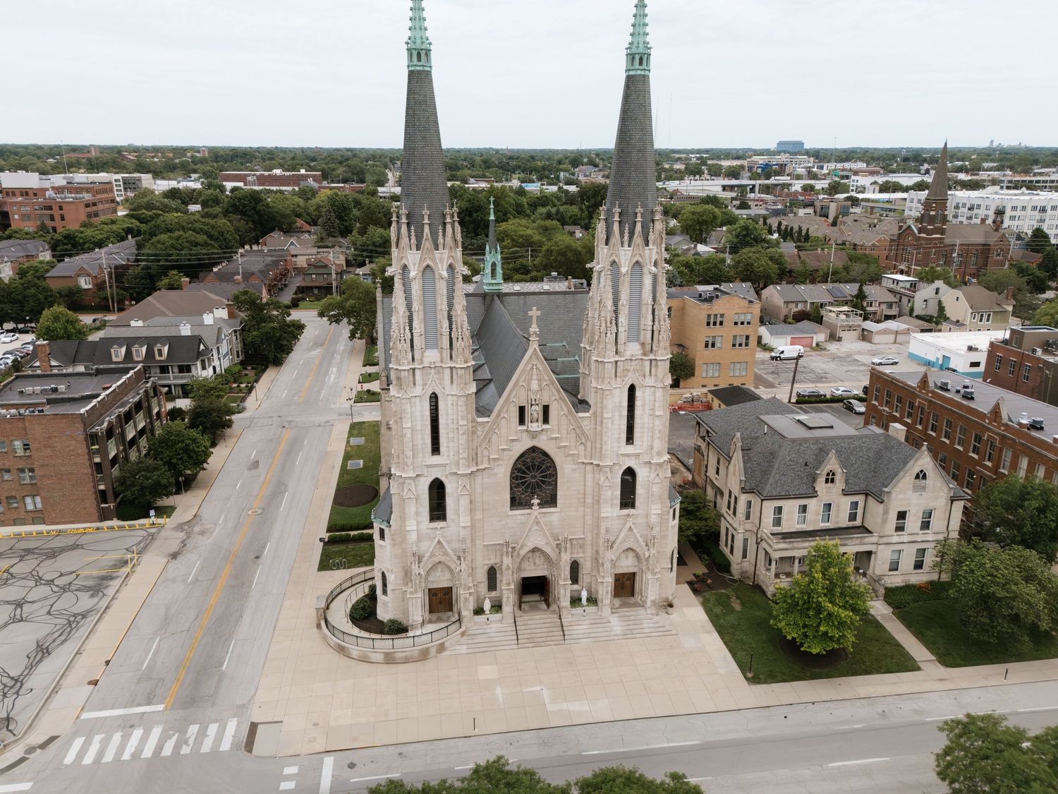 Aerial view of a Gothic-style church with twin spires in an urban neighborhood, surrounded by city streets and buildings.