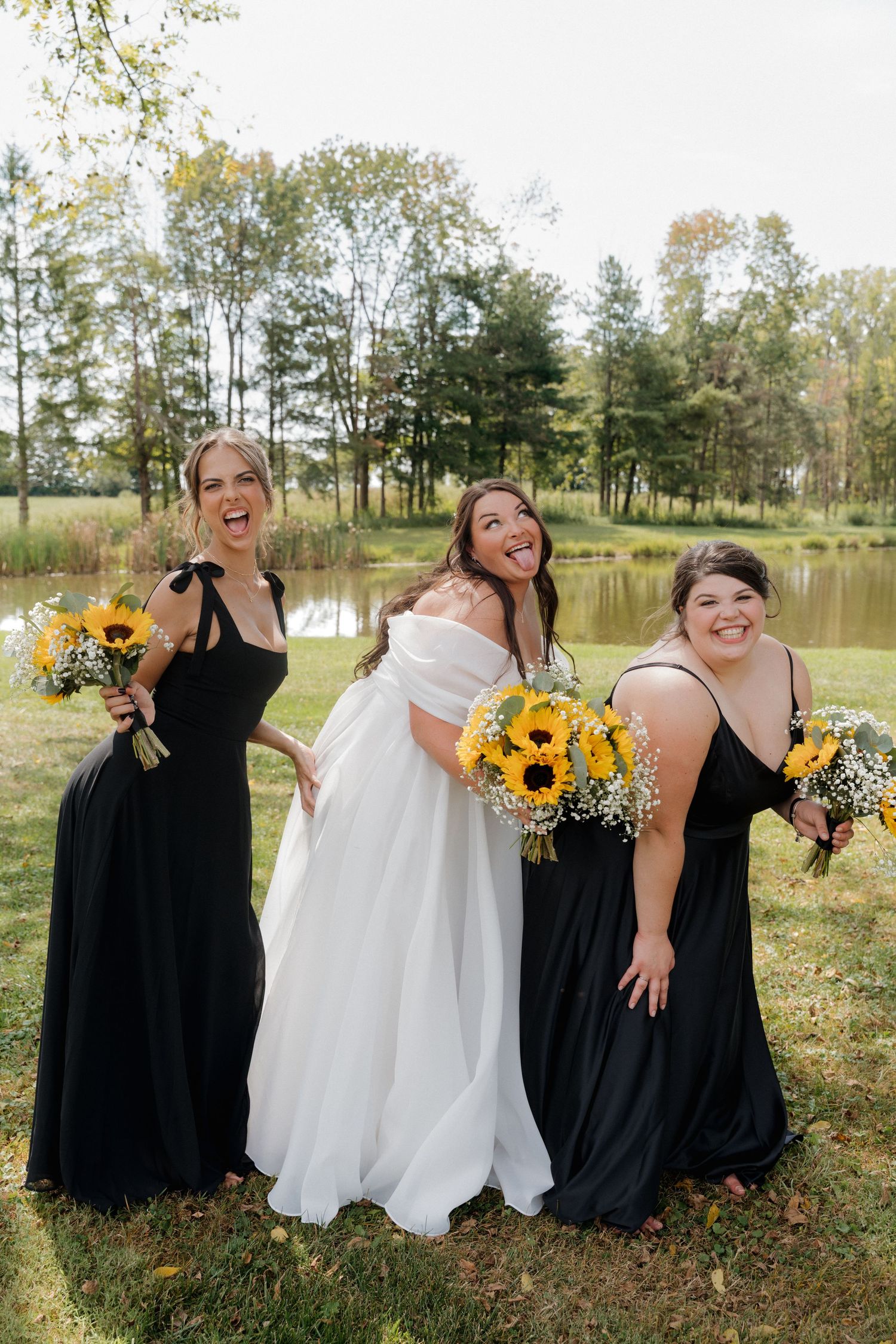 Bridal party in black and white dresses posing with sunflowers by a lake.