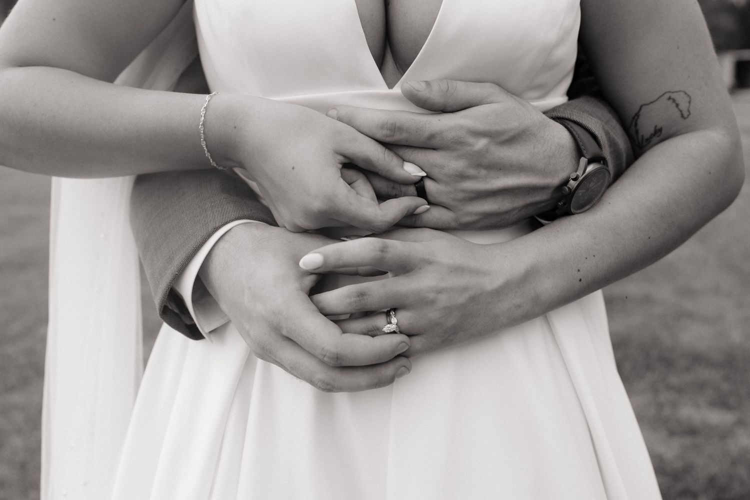 Black and white photo of newlyweds embracing, showing wedding rings on their intertwined hands.