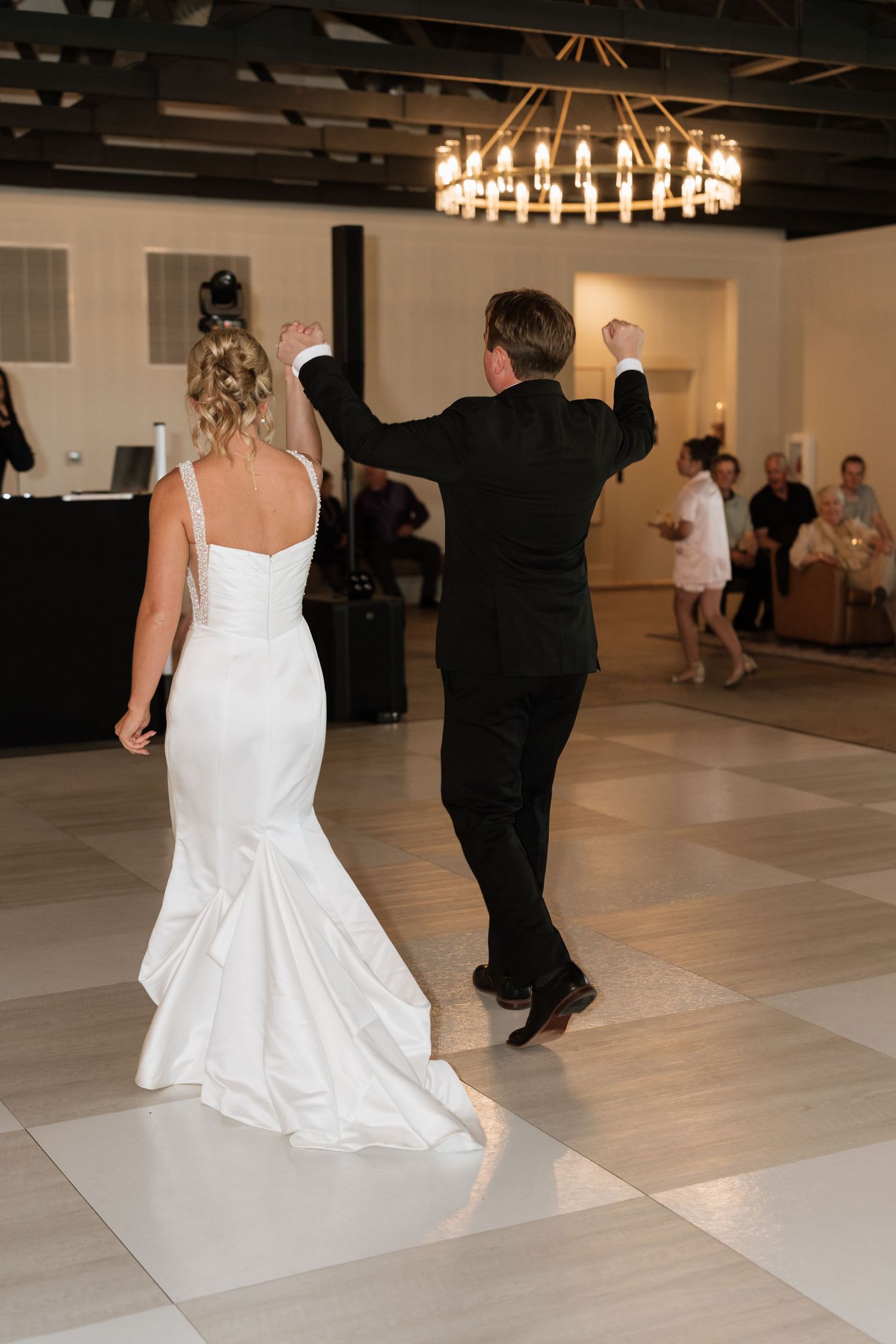 Bride in white gown and groom in black tux dance together on white floor at elegant wedding reception.