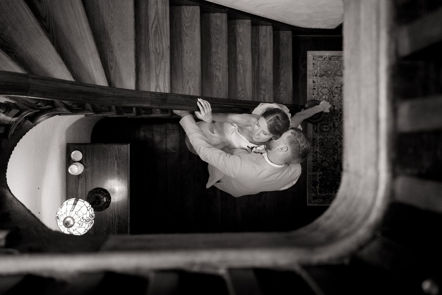 Black and white aerial photo of a couple embracing on a staircase landing, captured from above.