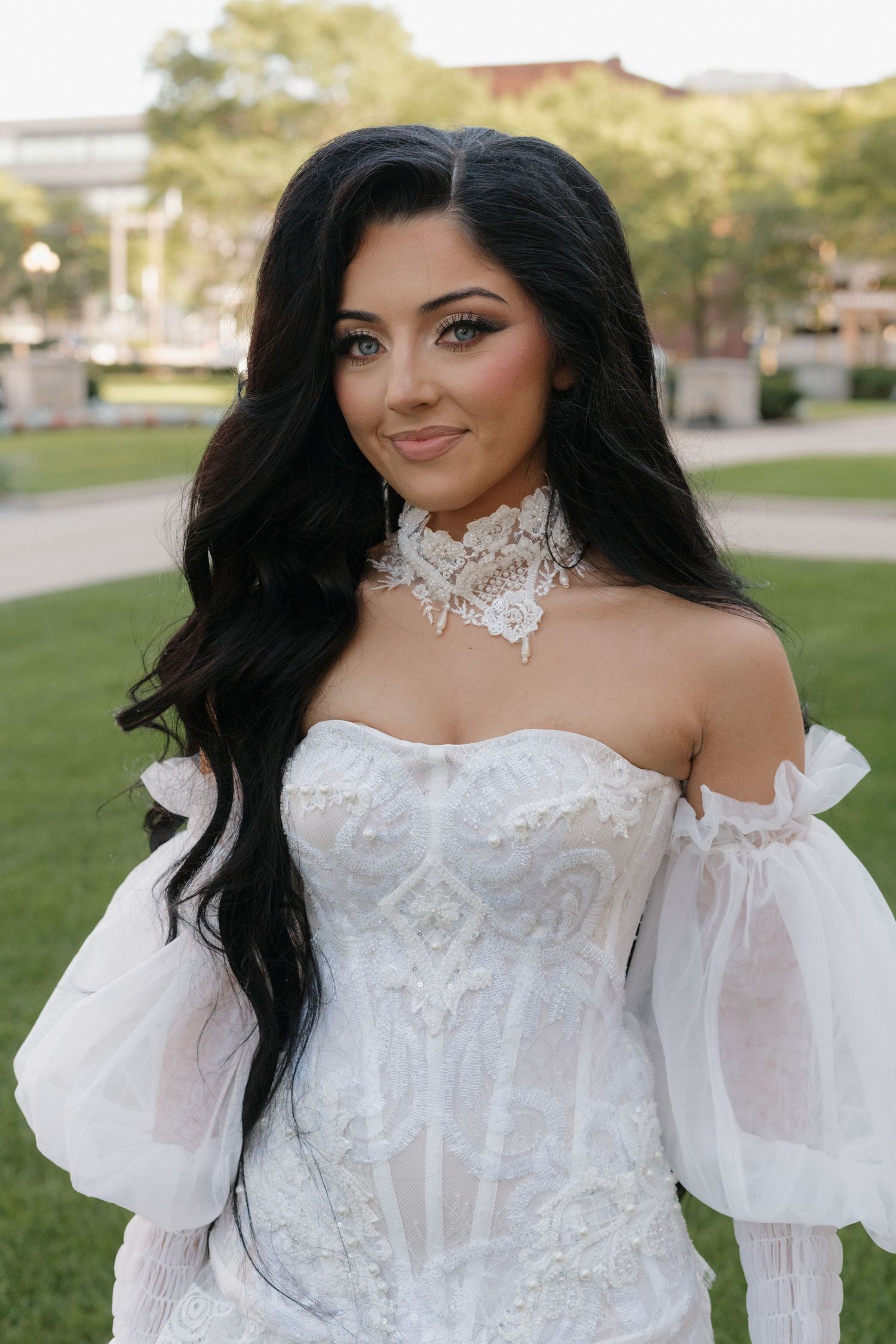 Bride in ornate white corset dress poses in outdoor setting.