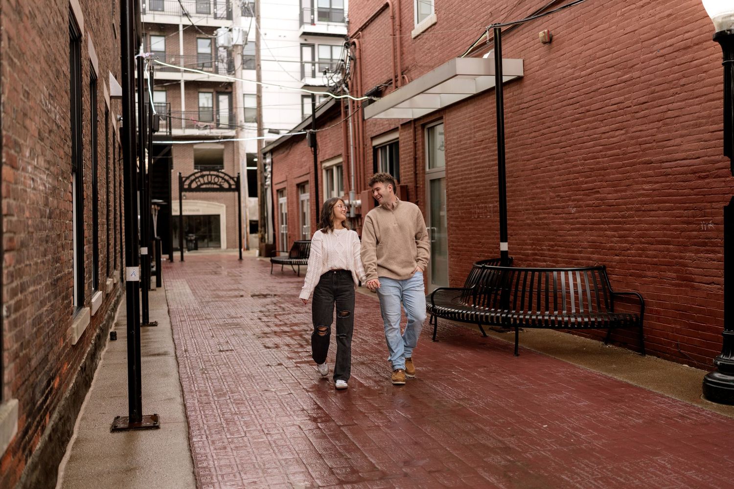 A couple walking together down a brick-paved street in an urban setting.