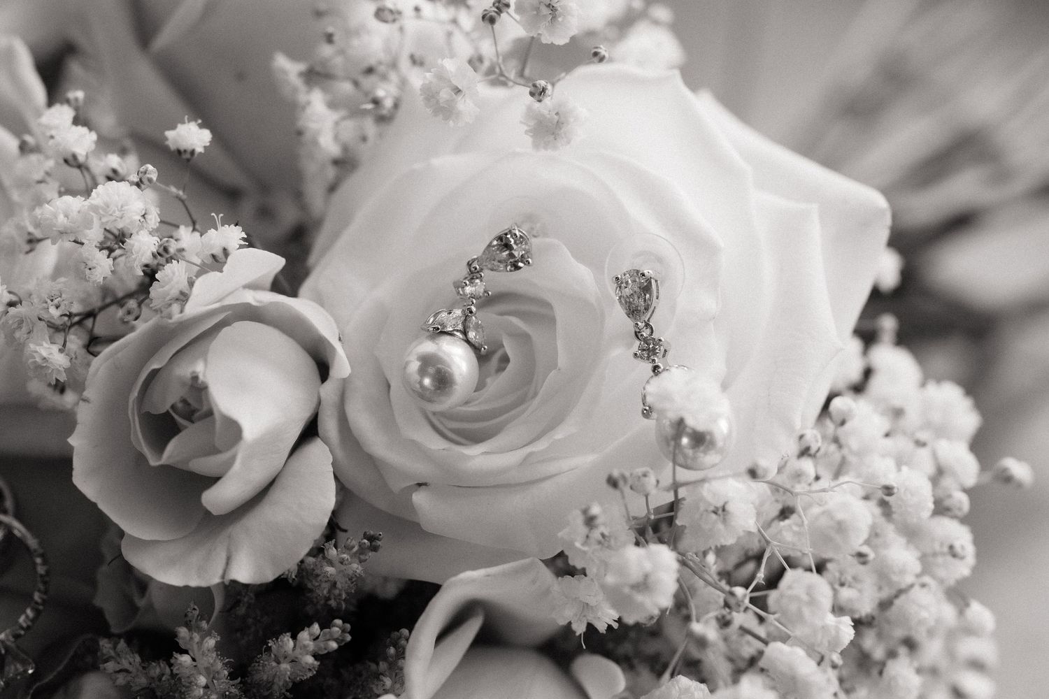 Black and white photo of white roses with pearl earrings nestled in a bridal bouquet with baby's breath.
