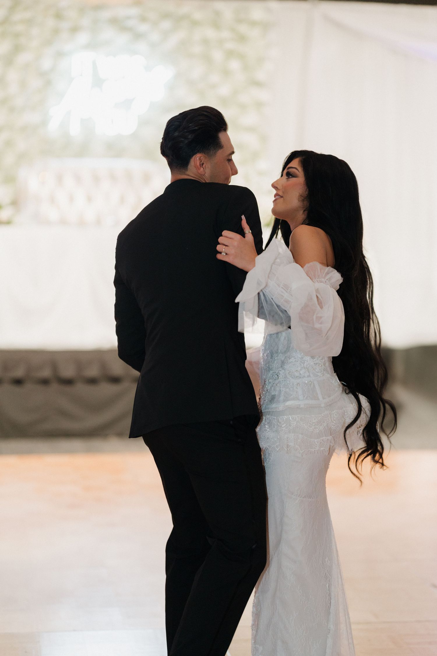 A couple shares a romantic dance together at their wedding reception in an elegant white-decorated venue.