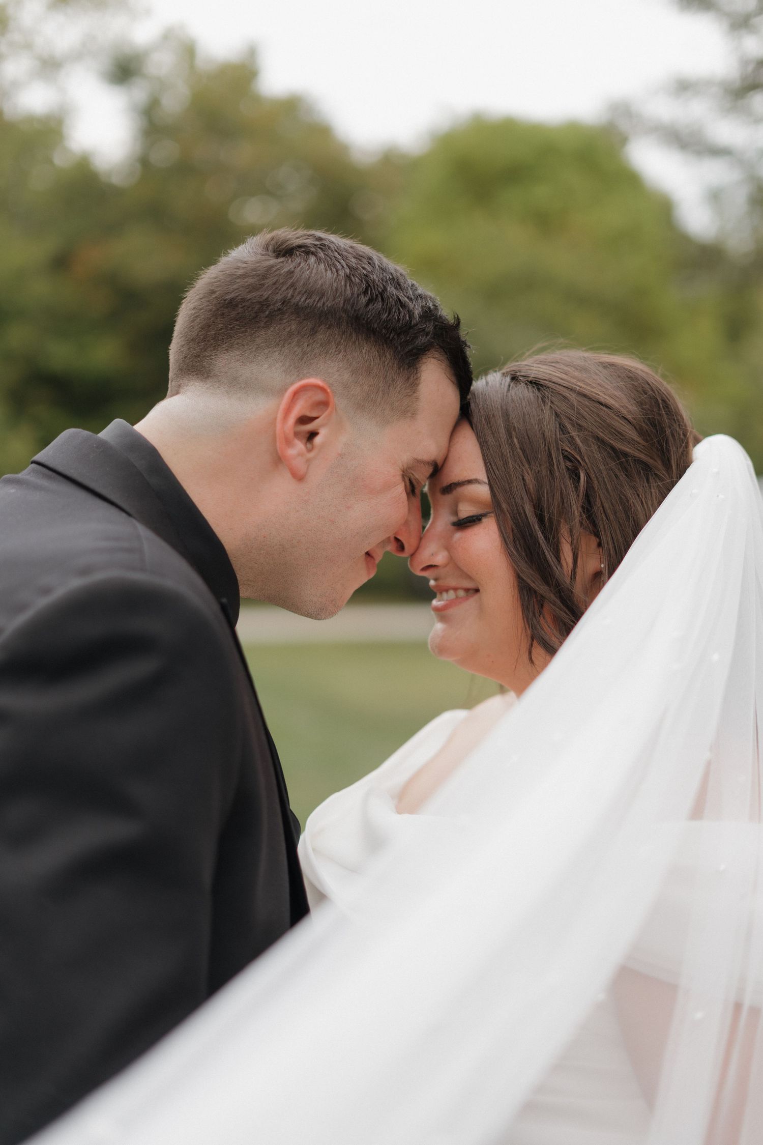 Romantic wedding couple shares intimate moment outdoors with flowing veil.