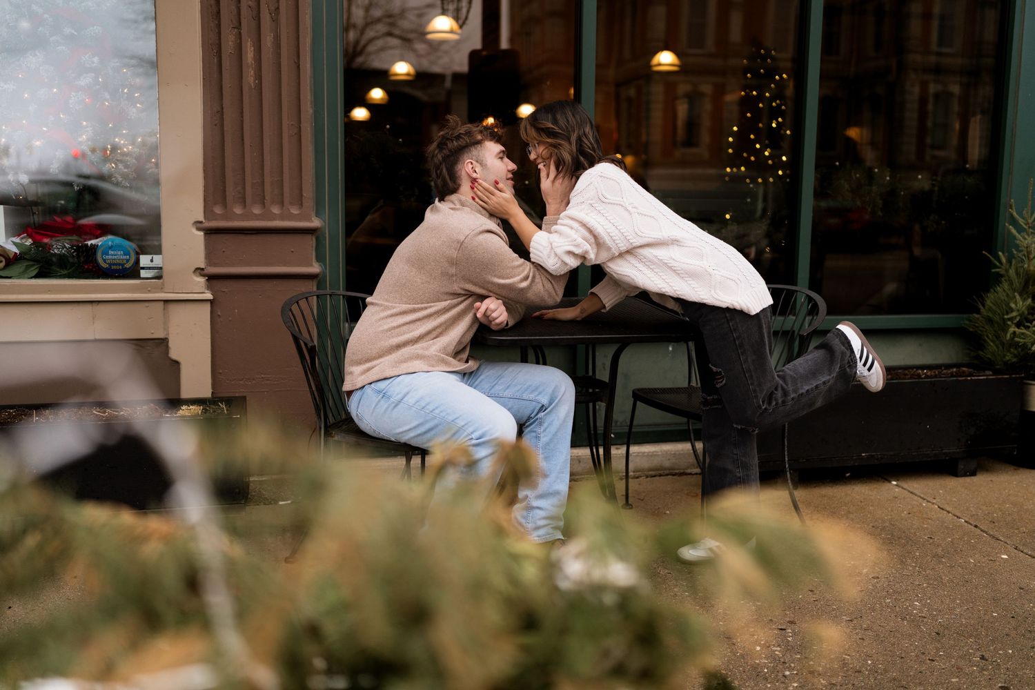 Couple sharing a tender moment outside a storefront with string lights.
