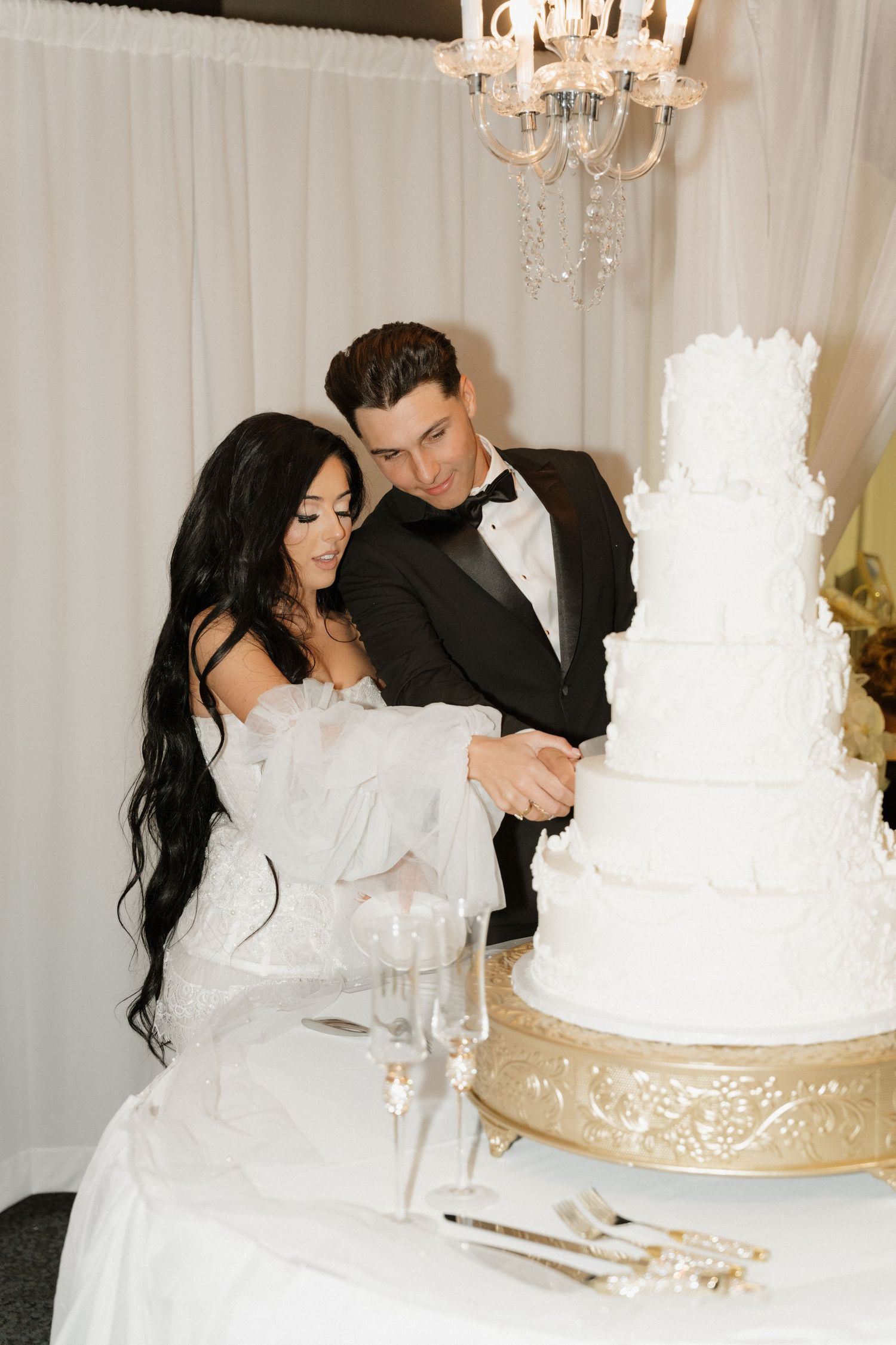 Newlyweds share an intimate moment next to their elegant white wedding cake at their reception.