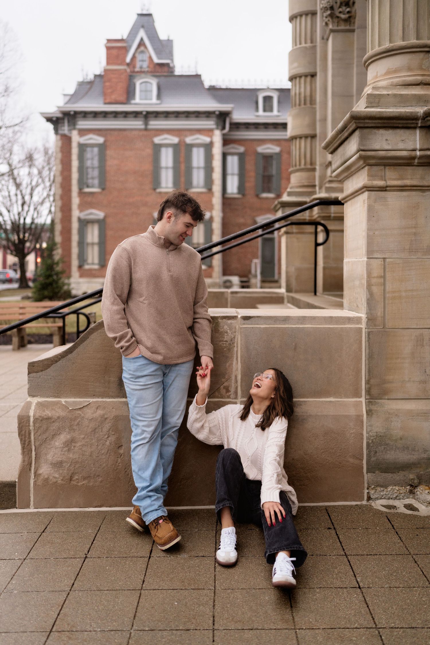 A couple interacting playfully on stone steps outside a historic building.
