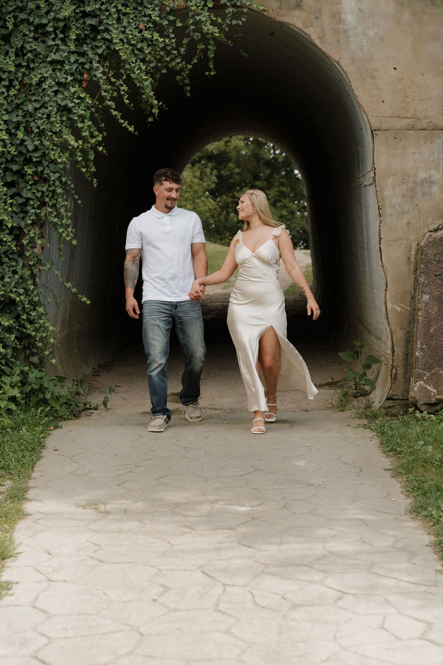 Couple walking through ivy-covered tunnel holding hands.