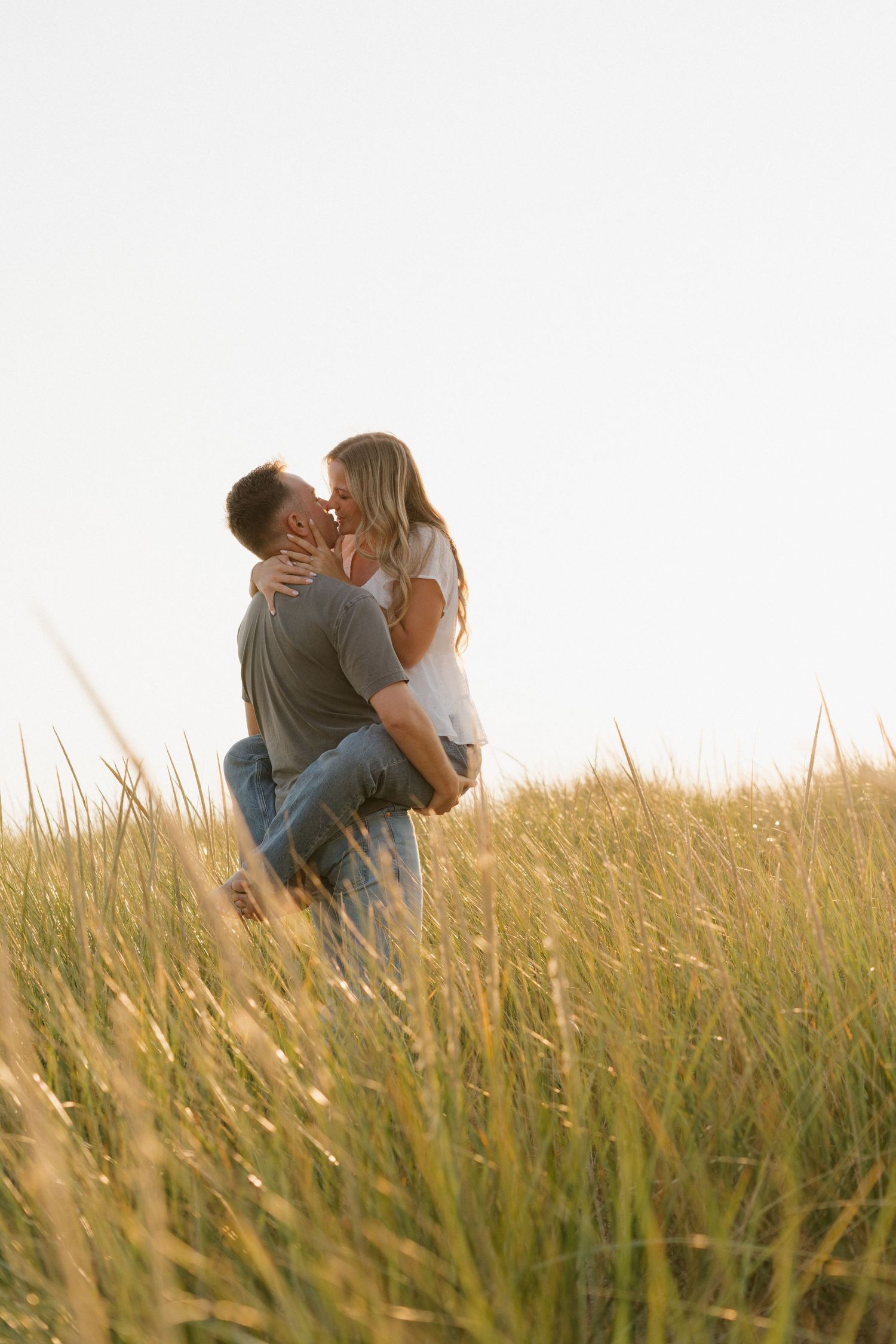 Intimate couple embracing in tall beach grass during sunset photo session.