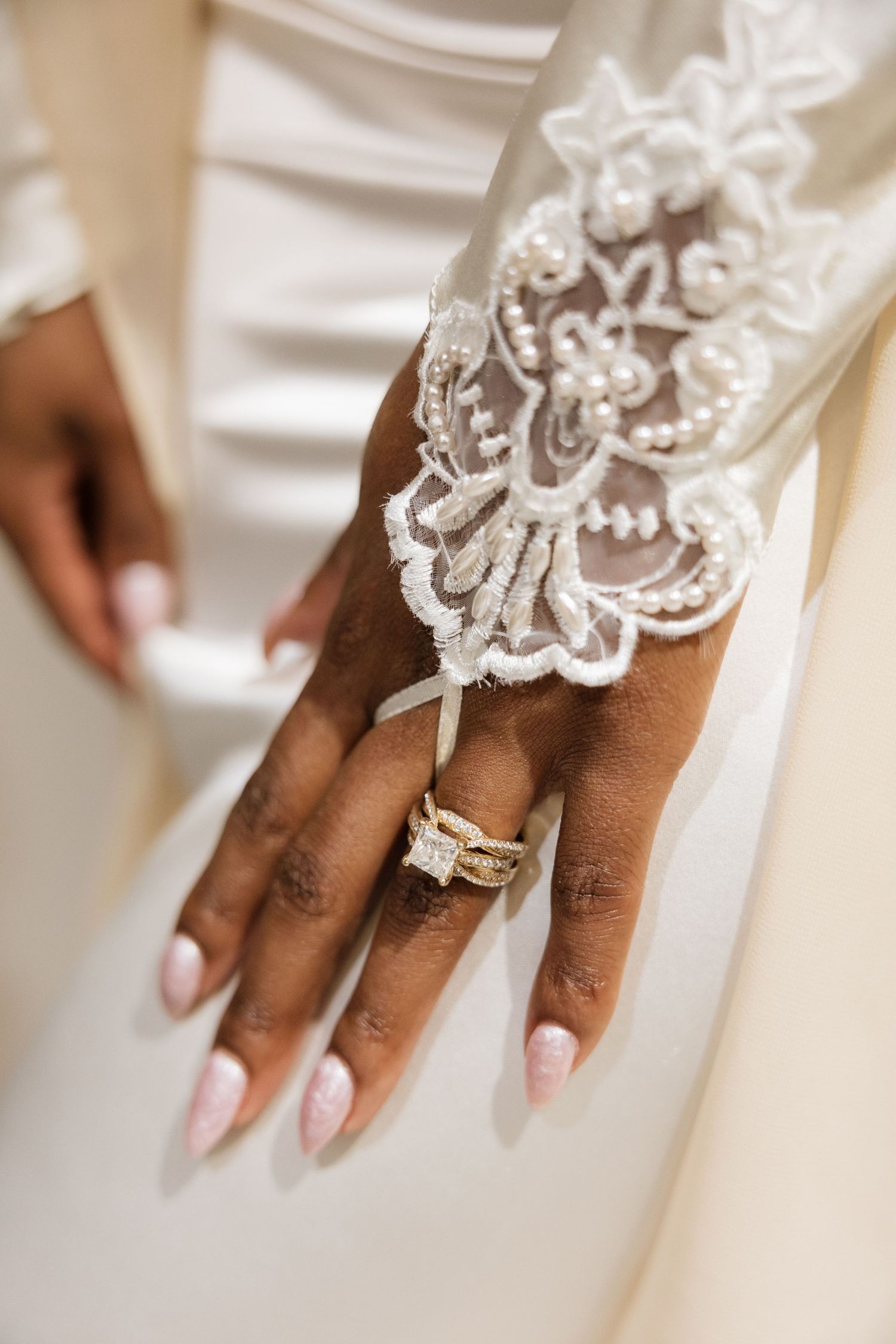 Close-up details of lace wedding dress and jewelry on hands.