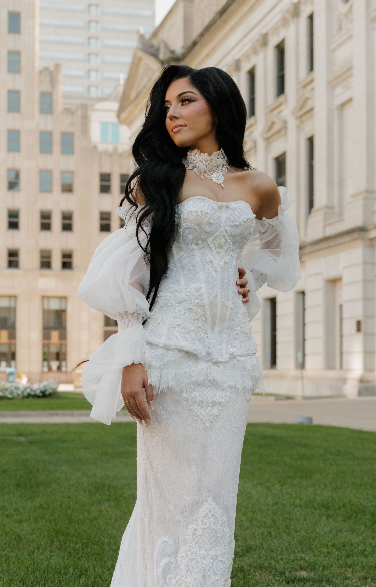 Bride in detailed white gown poses against classical architecture.