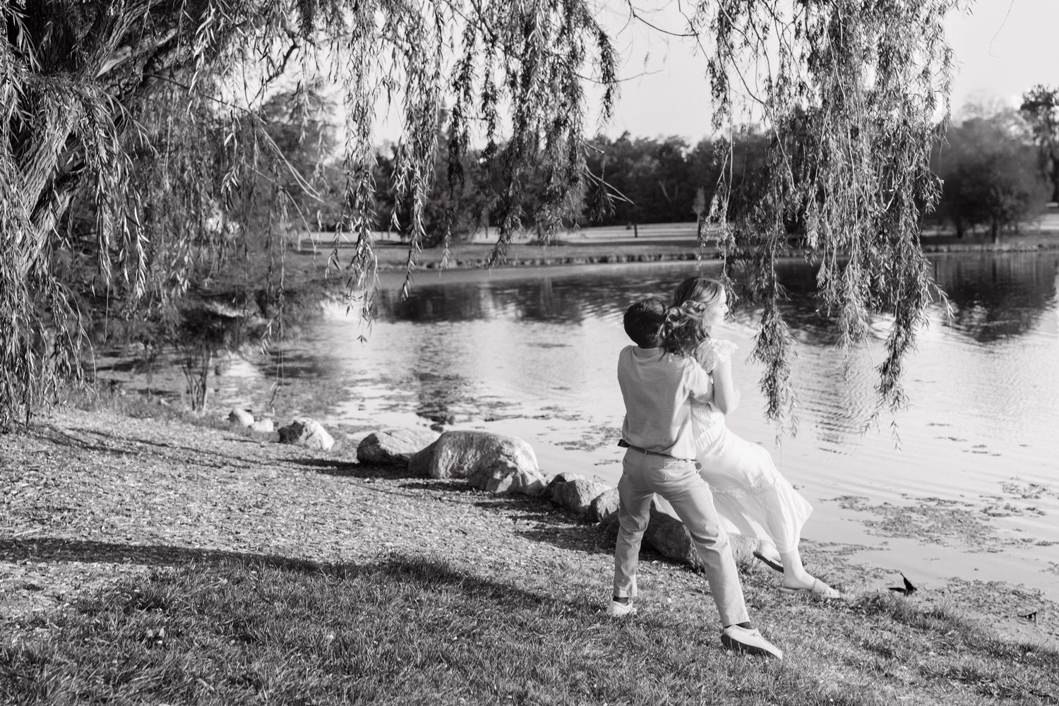 A black and white photo of a couple walking together near a lake with willow trees. cox hall gardens, Indianapolis