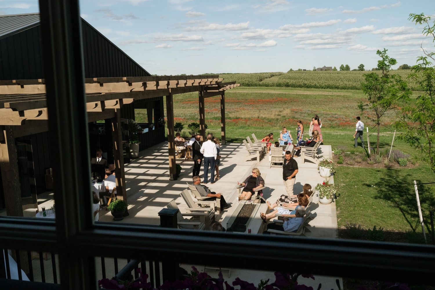 Guests mingle on a modern outdoor patio overlooking open fields at a winery or event venue.