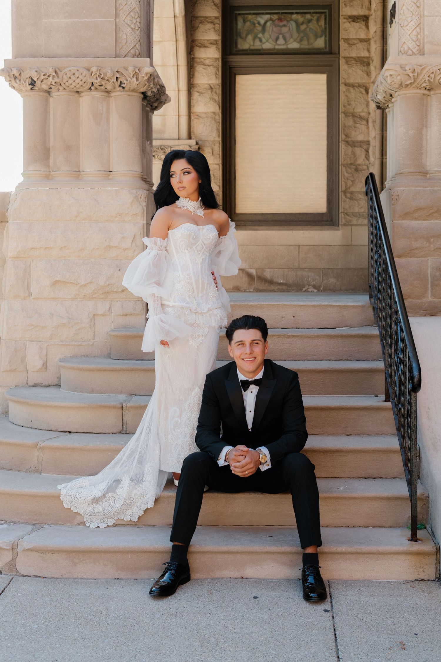 Wedding couple poses creatively on stone steps of historic building.