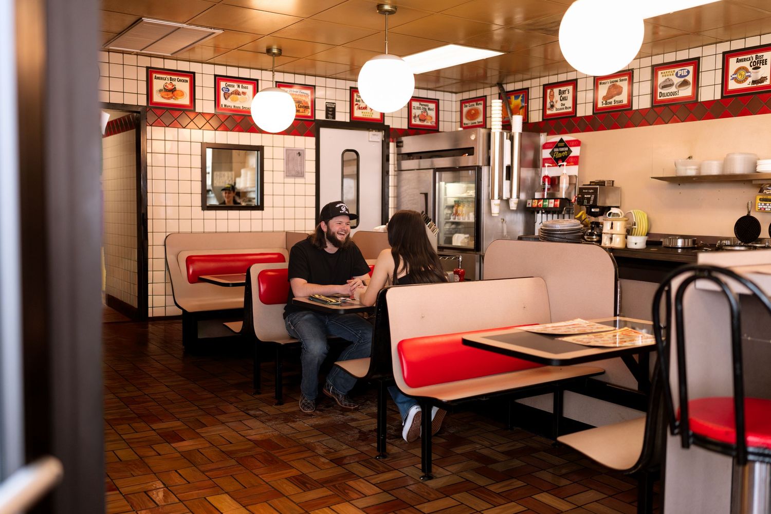 Interior of a classic American diner with red booths and framed pictures on wood paneled walls.