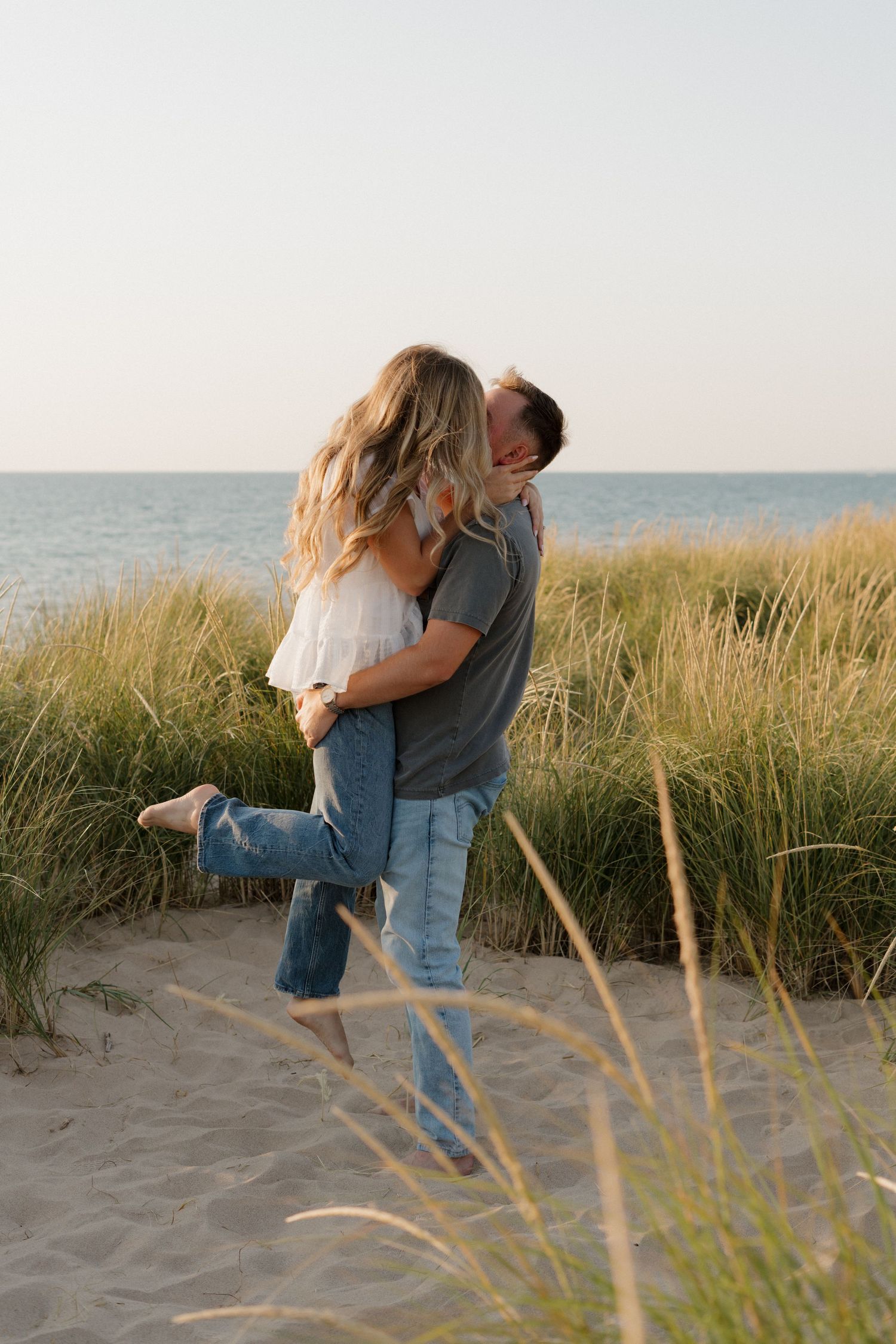 A romantic embrace on a beach at sunset with tall grass and ocean in the background.  engagement session, lifestyle, indianapolis, ocean