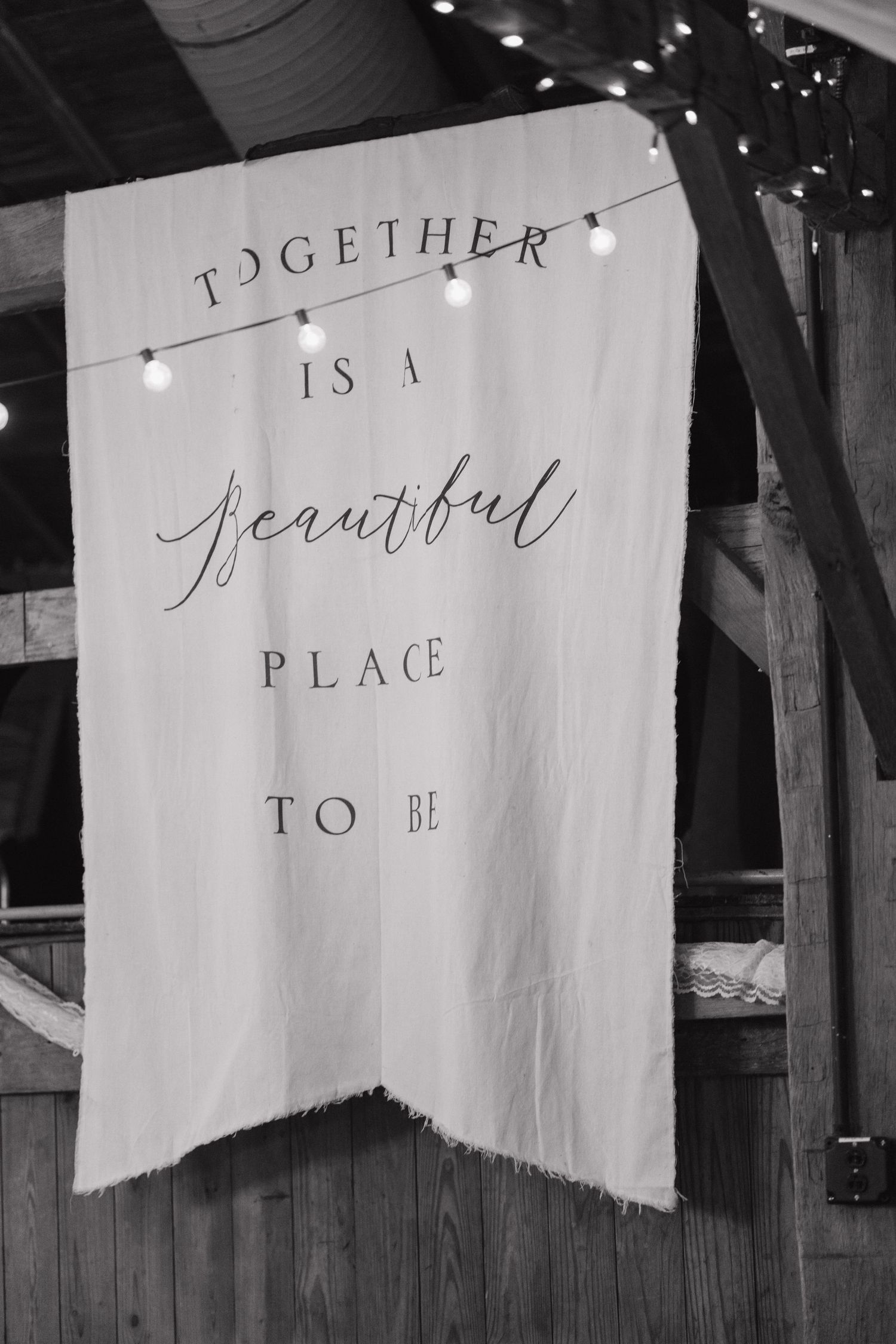 Black and white banner signs with romantic text hanging from rustic wooden beams with string lights.