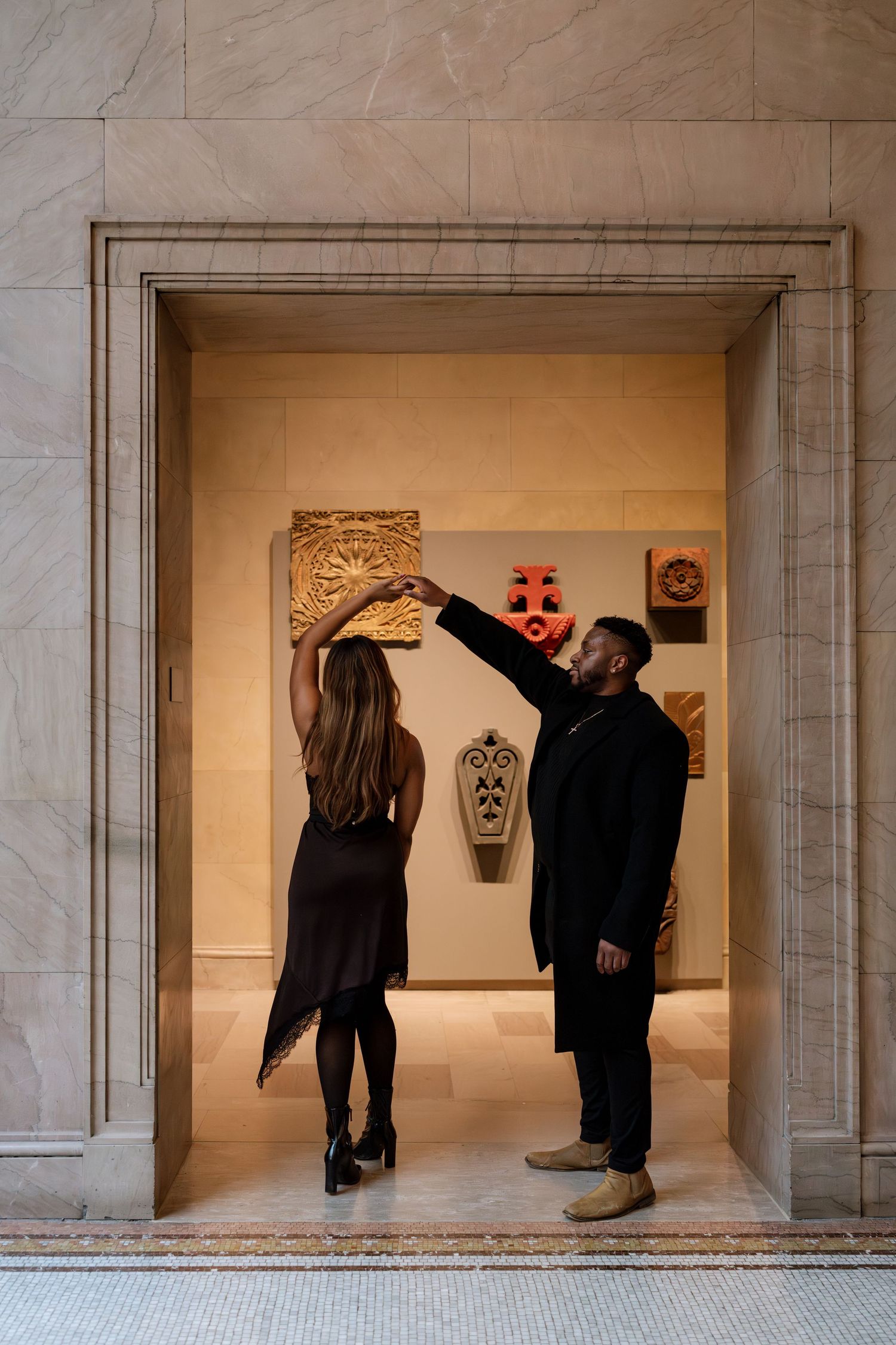 Gallery visitors observe artwork displayed in three illuminated alcoves along a marble wall.