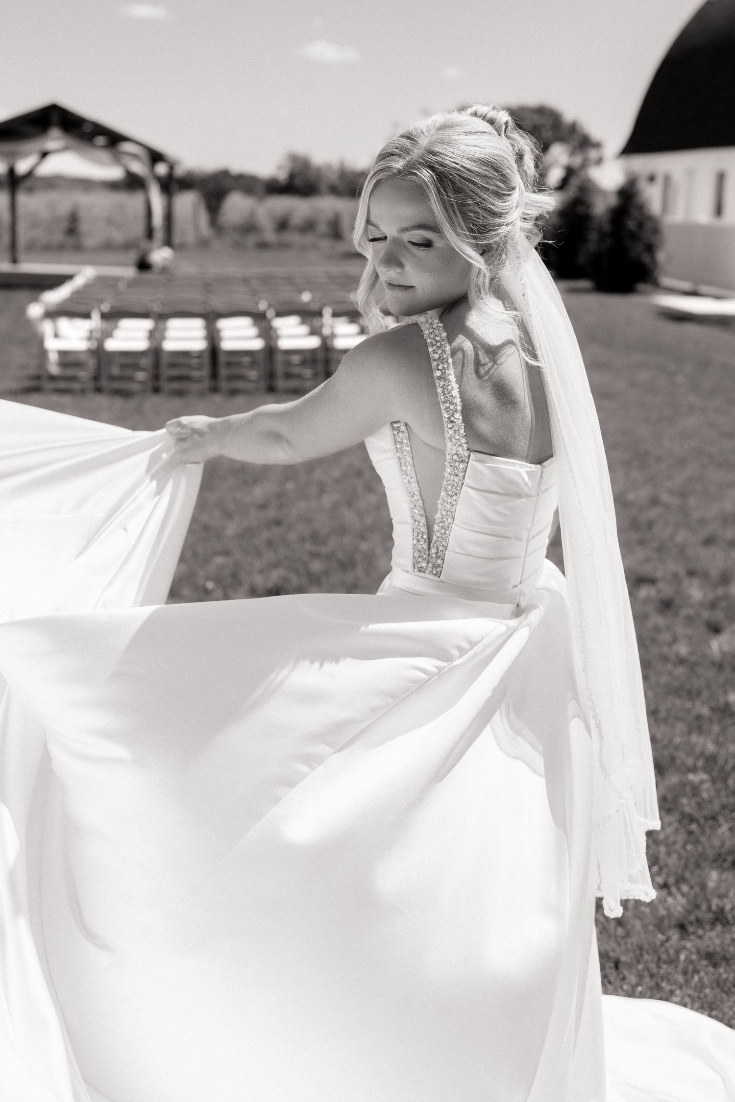 Black and white photo of a bride in a strapless gown with veil, gracefully holding her flowing dress outdoors.