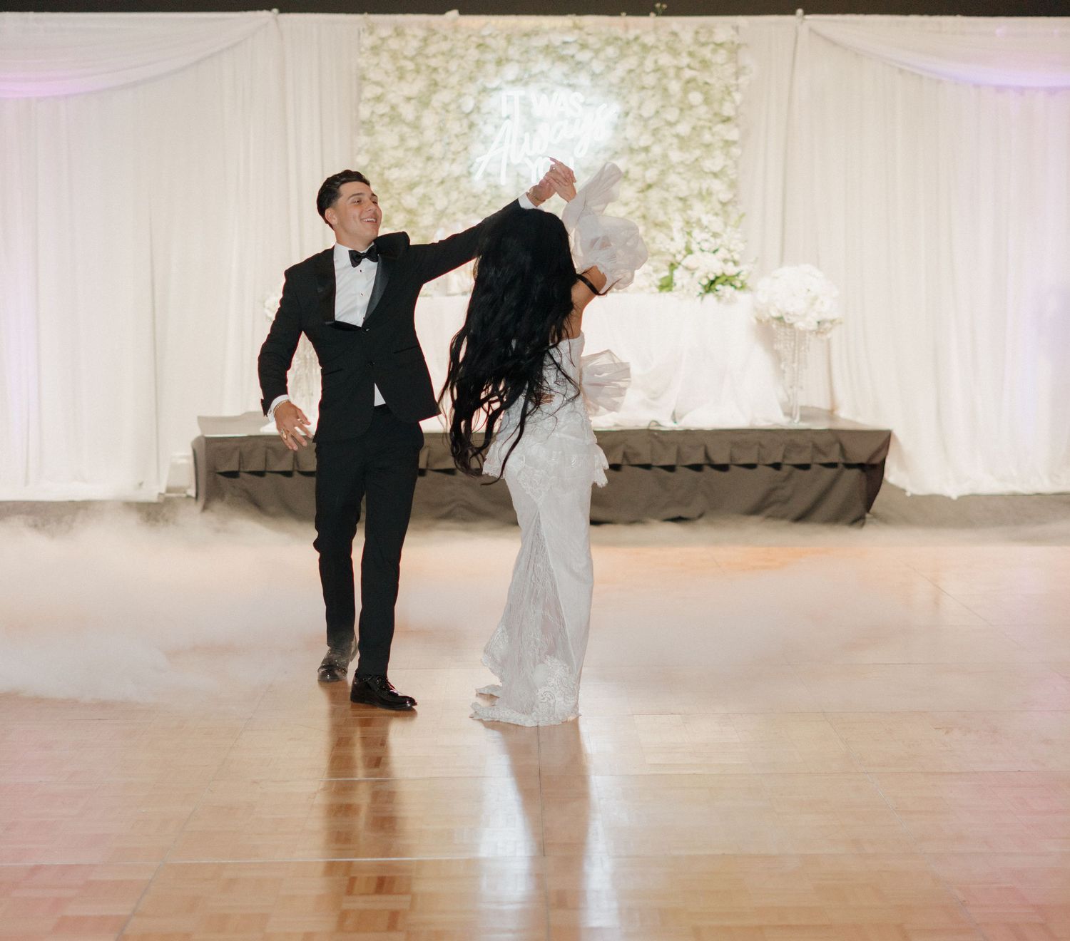 A couple performs a romantic dance sequence in a white-decorated ballroom setting.