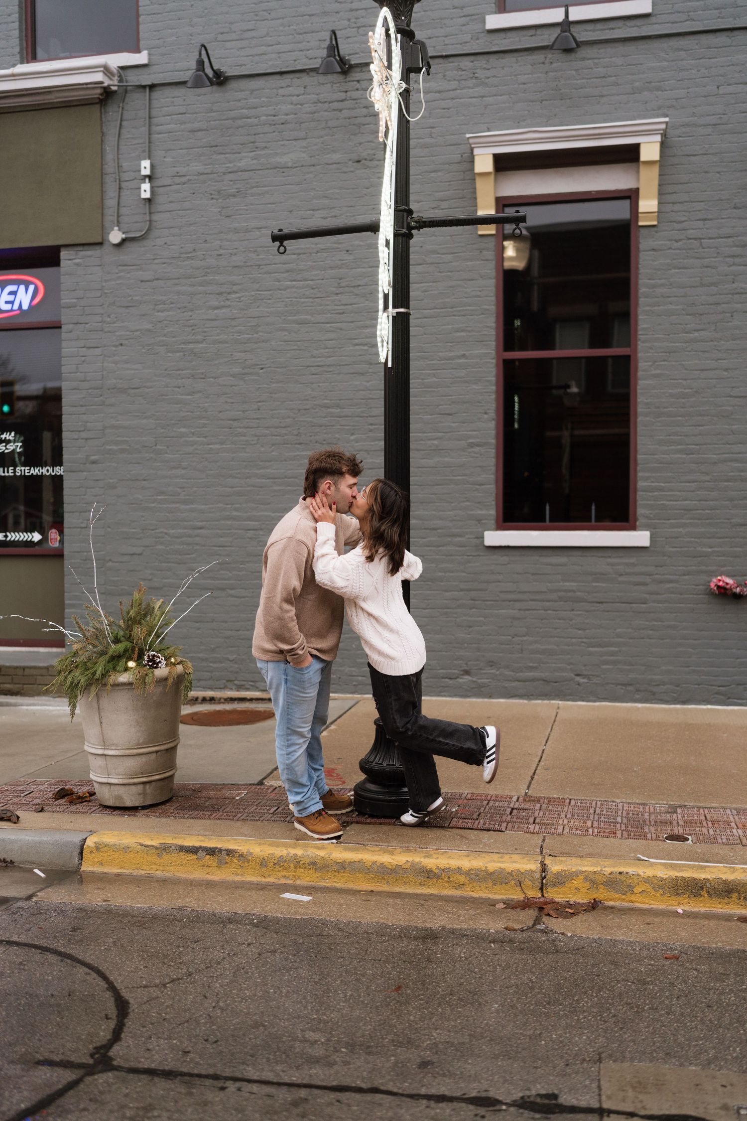 Two people sharing an intimate moment on a sidewalk near a grey building.