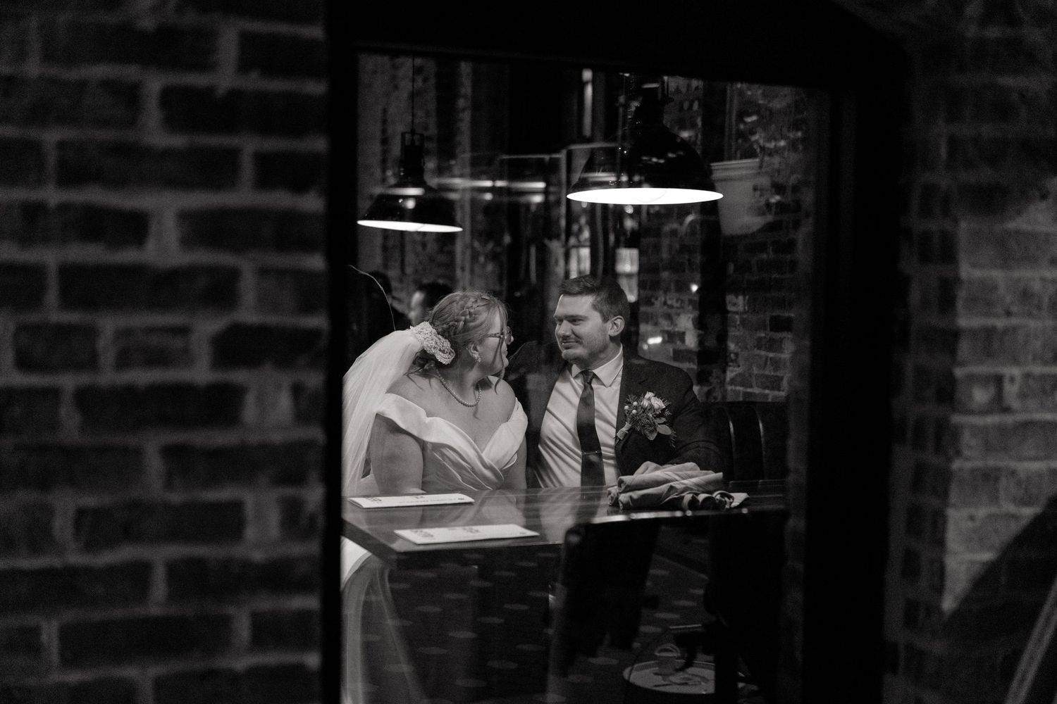 Wedding couple poses in front of brick wall with industrial lighting.