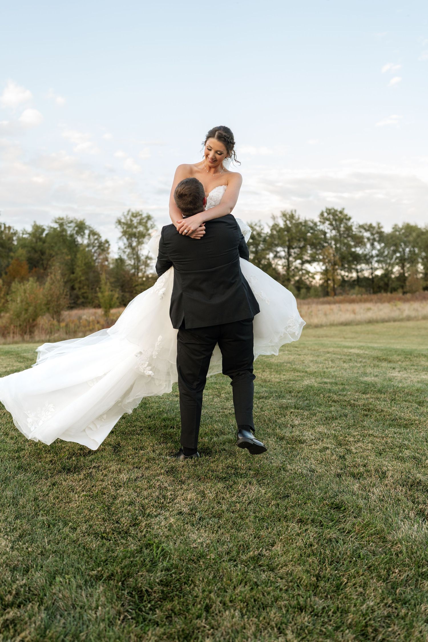Joyful wedding moment with couple embracing on grassy field.