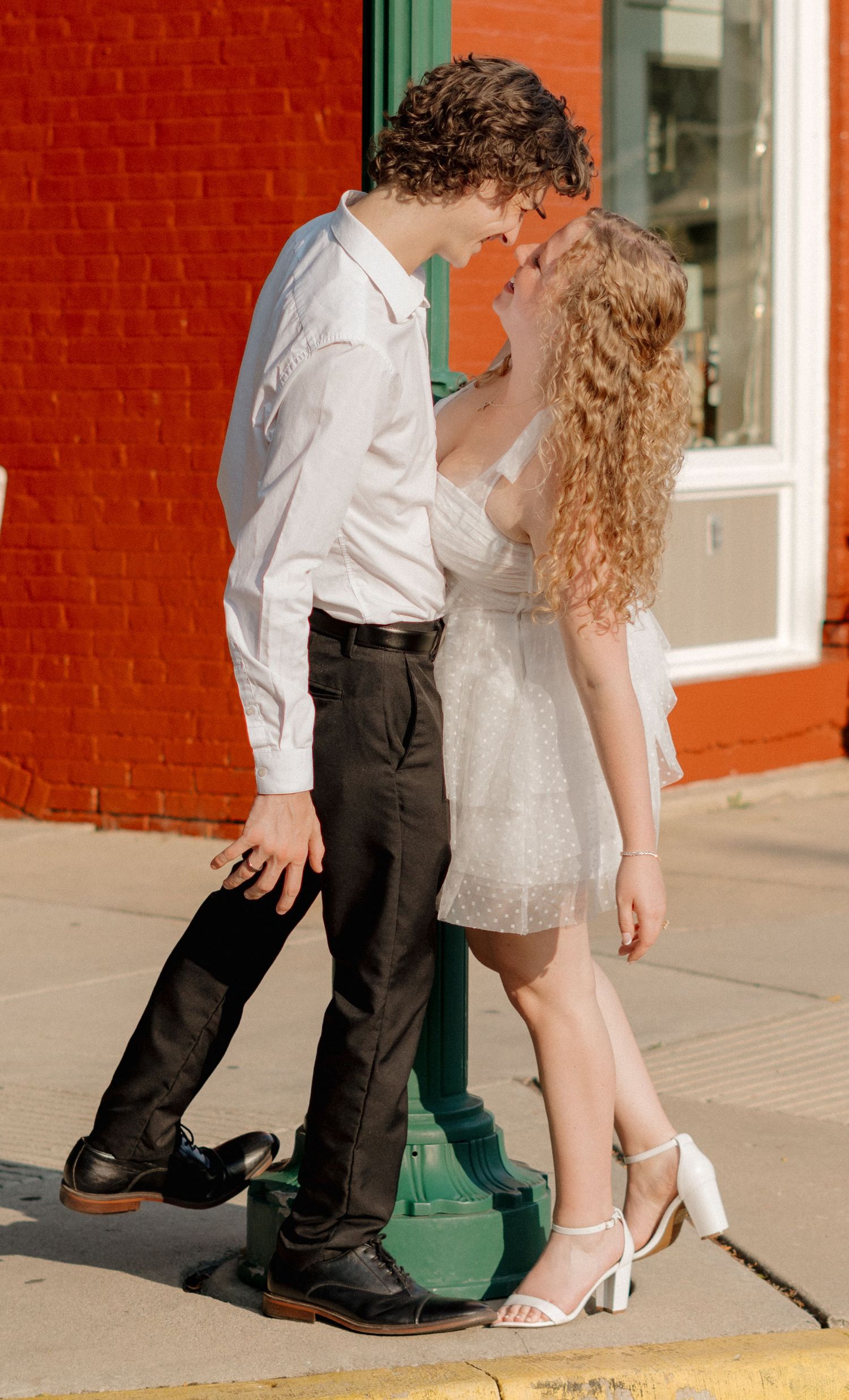 A couple in formal attire poses for a series of romantic dance-inspired photos against a brick wall.