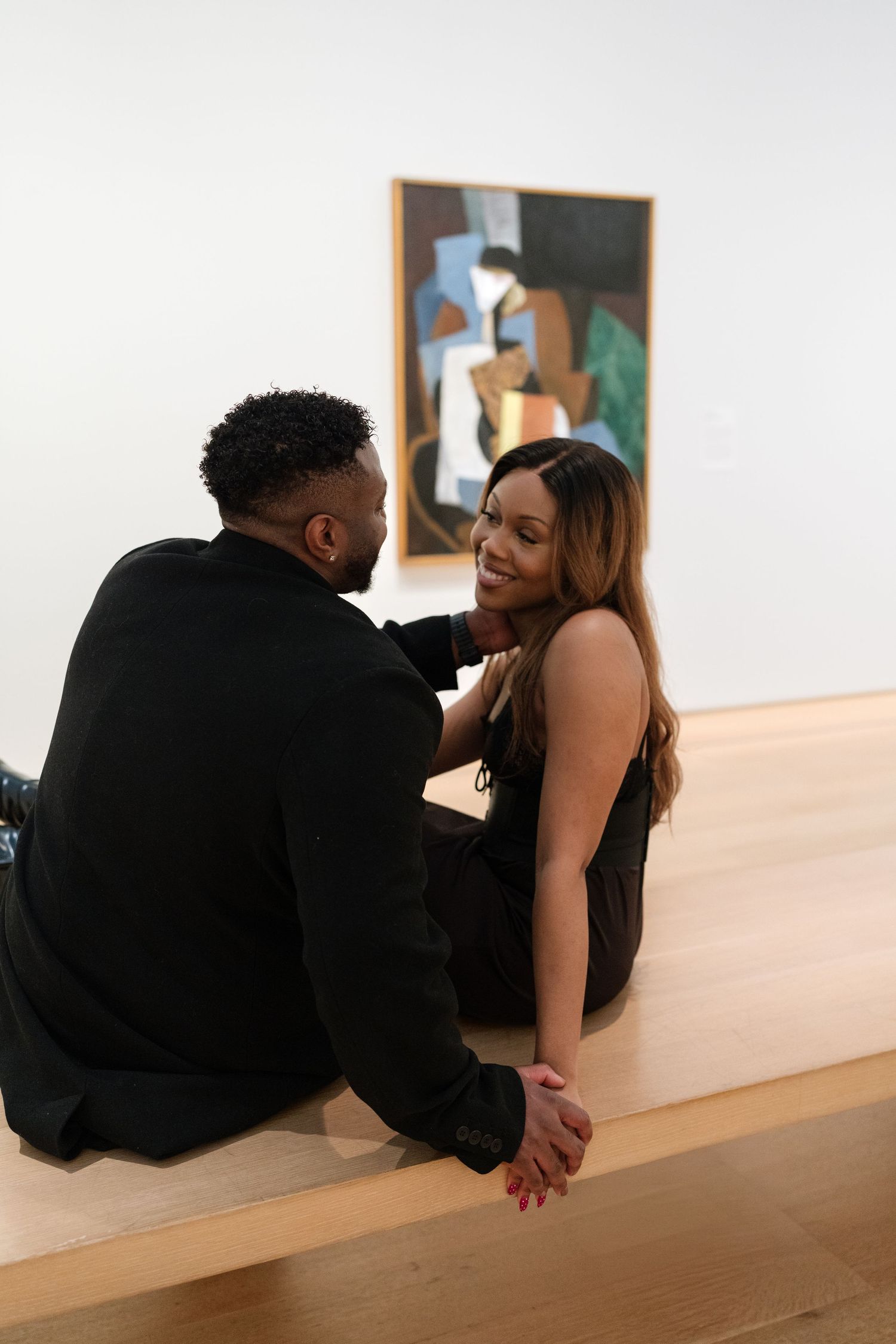 A couple shares an intimate moment while sitting in an art gallery with a modern painting displayed on the wall.