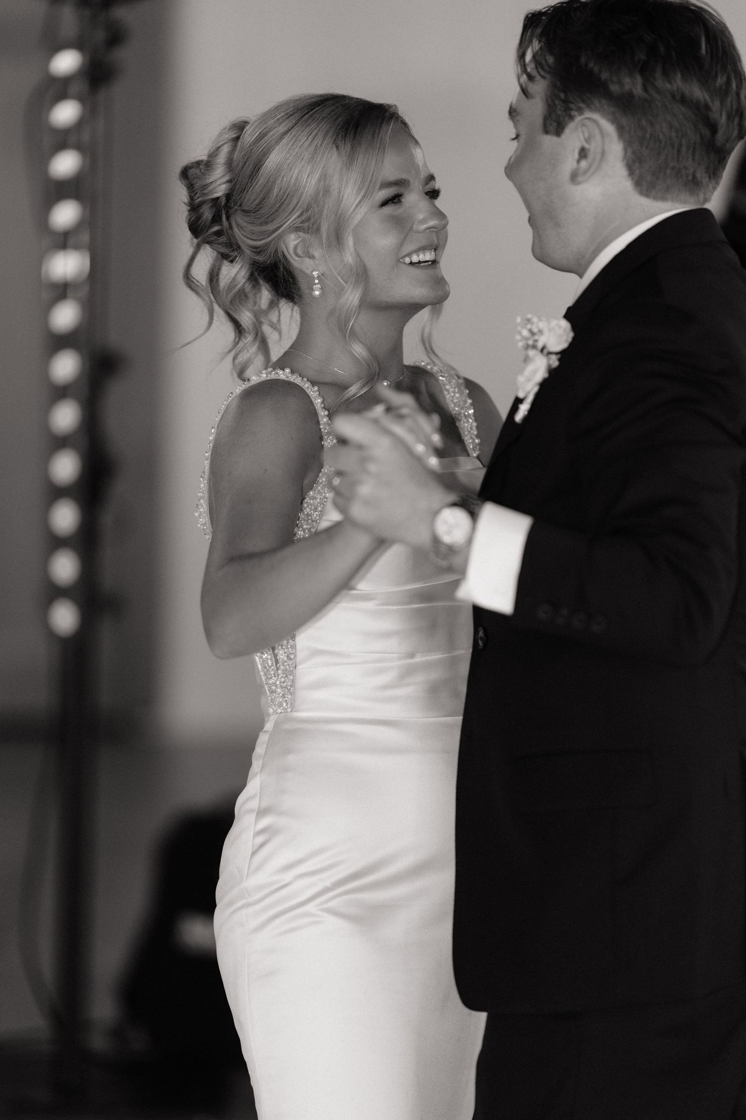 Black and white photo of a bride and groom sharing their first dance, smiling joyfully at their wedding reception.