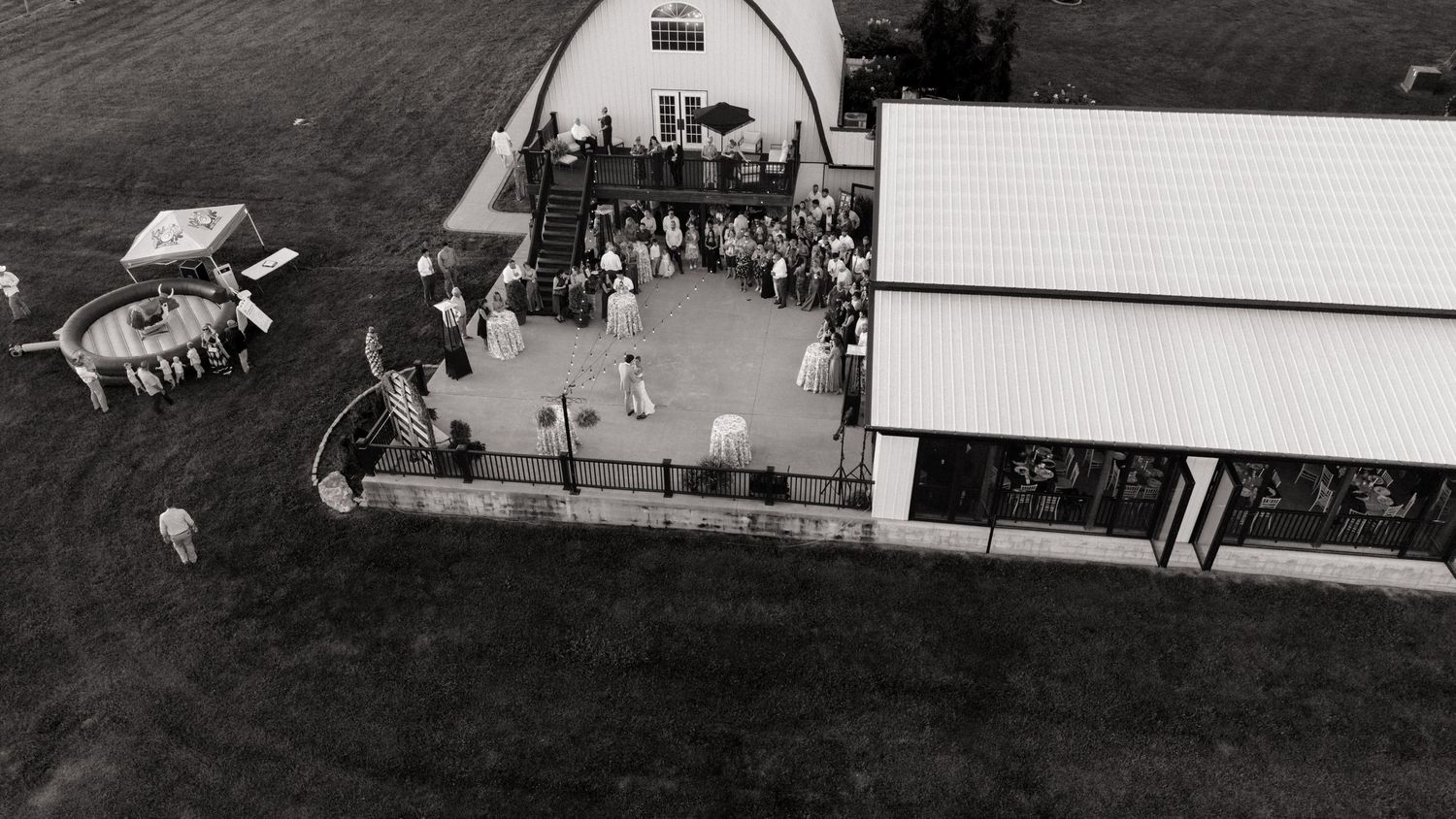 Aerial black and white photo of a barn wedding venue with guests gathered outside on a sunny day.
