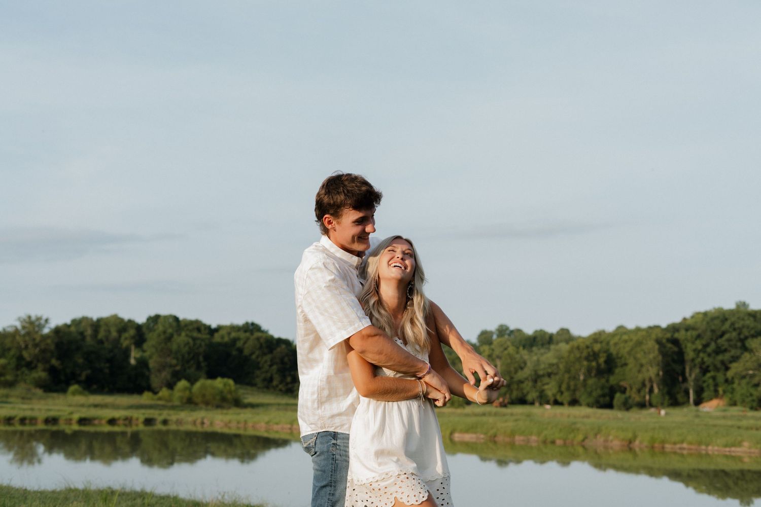 A couple embraces by a scenic lake during golden hour.