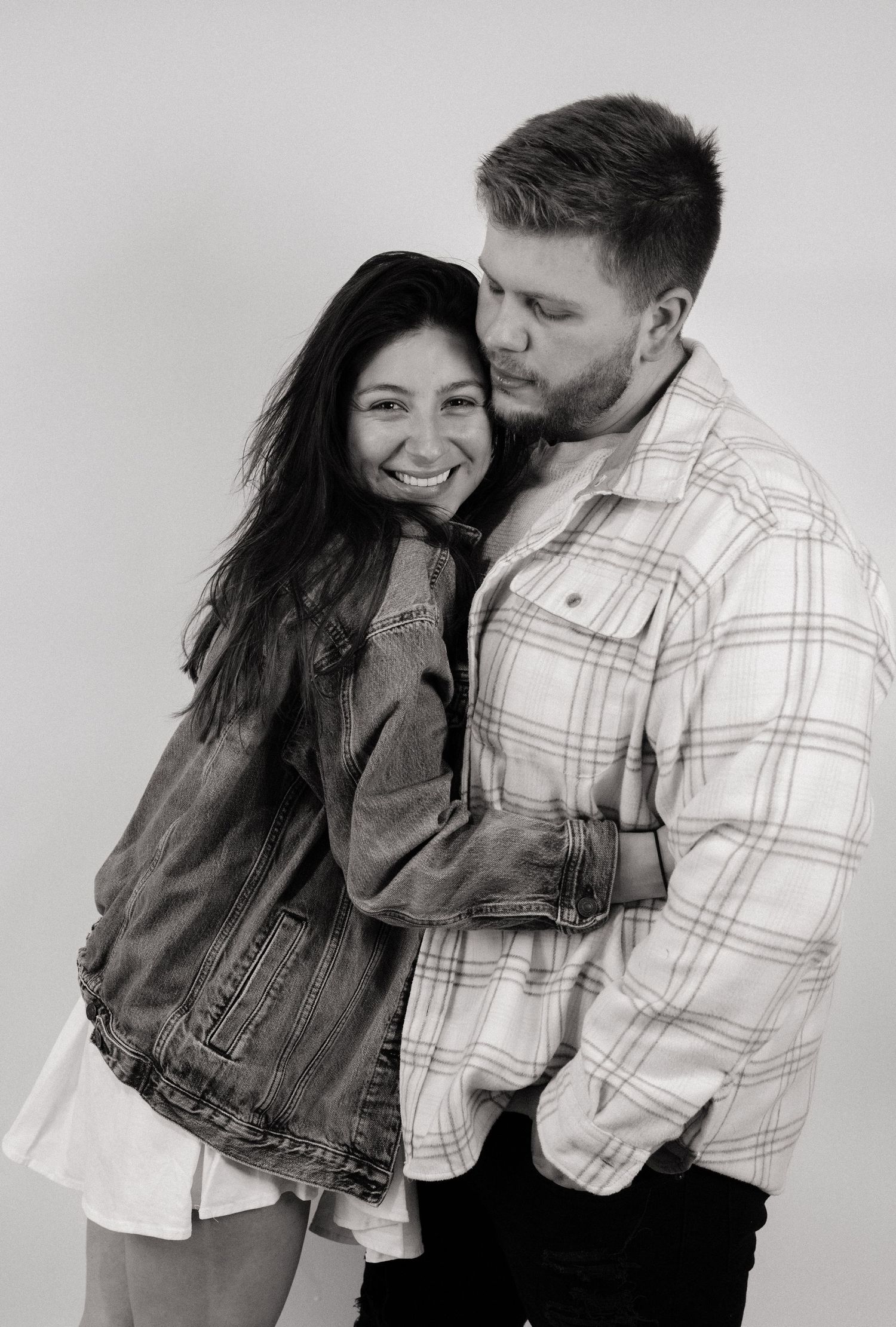 A candid black and white portrait of a couple embracing and laughing while wearing casual attire.