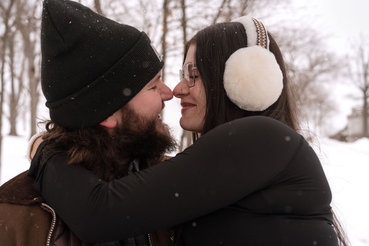 Two people in winter clothing sharing an intimate moment in a snowy setting.