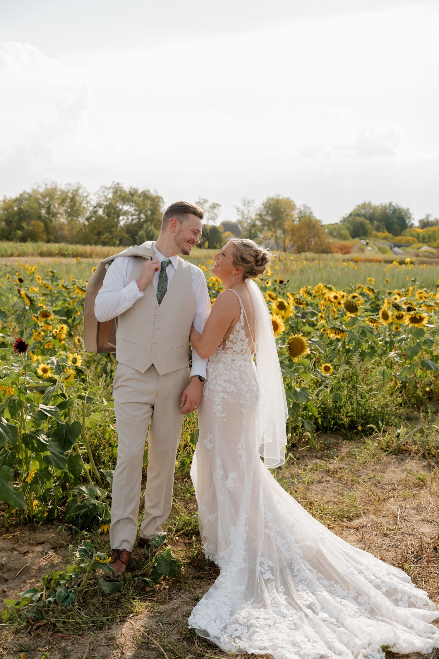Newlyweds share intimate moments in a sunflower field wearing white wedding attire.