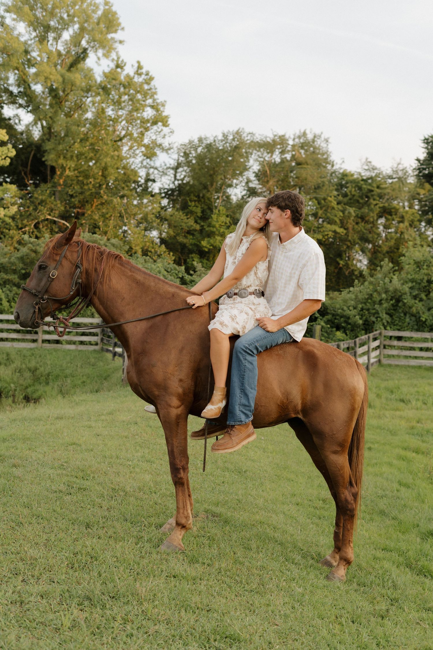 A romantic horseback photoshoot in a green pasture with white fencing.